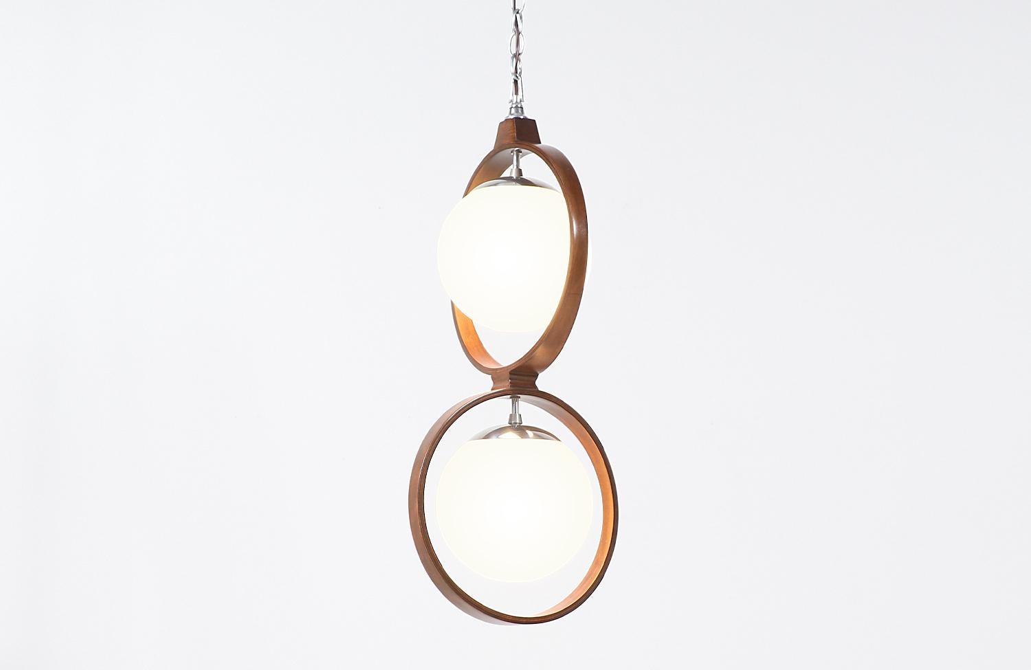 Dazzling Mid-Century Modern pendant chandelier designed by Arthur Jacobs for Modeline in the United States, circa 1970s. This expertly crafted walnut bentwood pendant features two wooden rings with its original frosted glass globes hanging from a