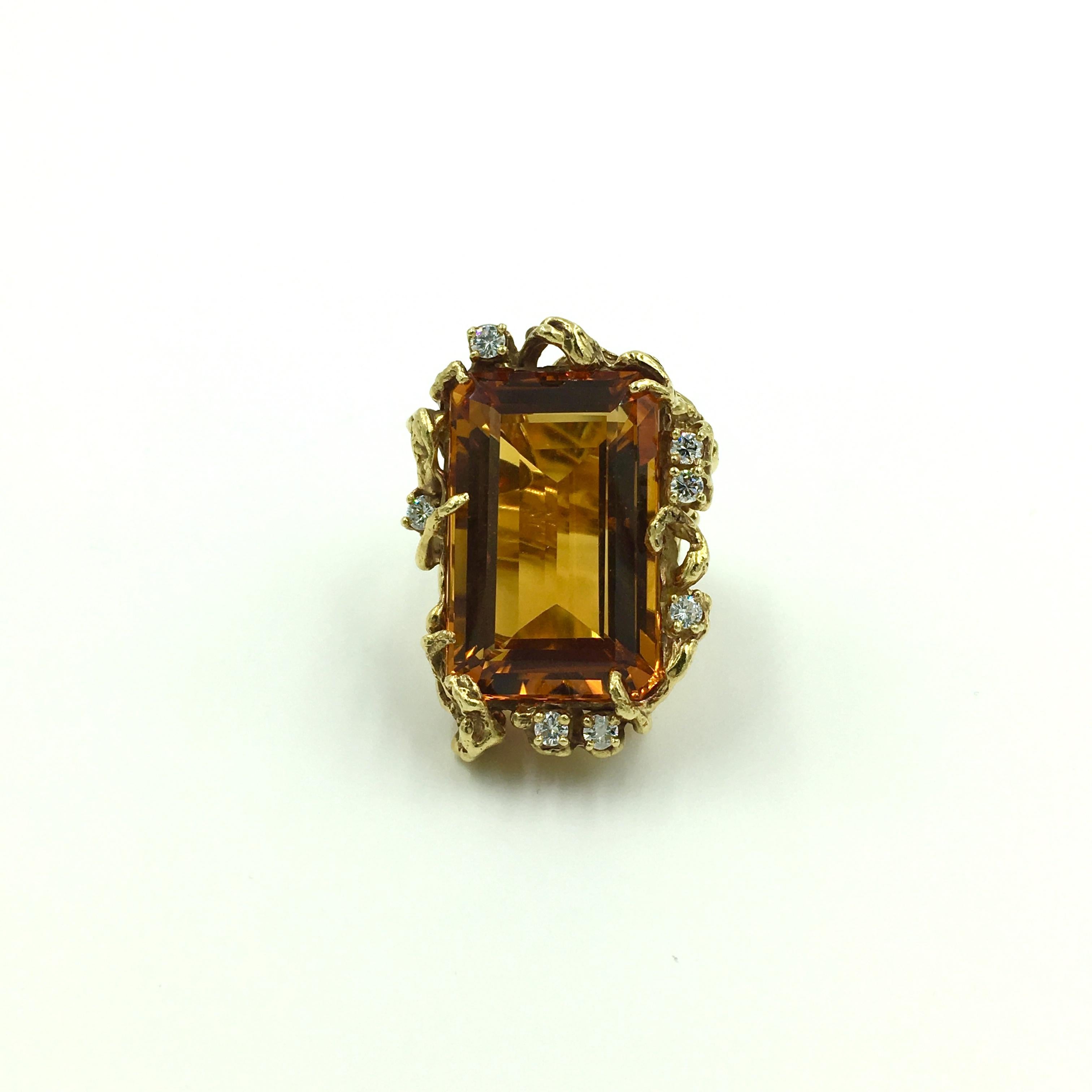 An 18 karat yellow gold, citrine and diamond ring. Arthur King, Circa 1970. Set asymmetrically with an emerald cut golden orange citrine, measuring approximately 25.00 x 17.00 x 10.50mm, and weighing approximately 29.65 carats, within a textured