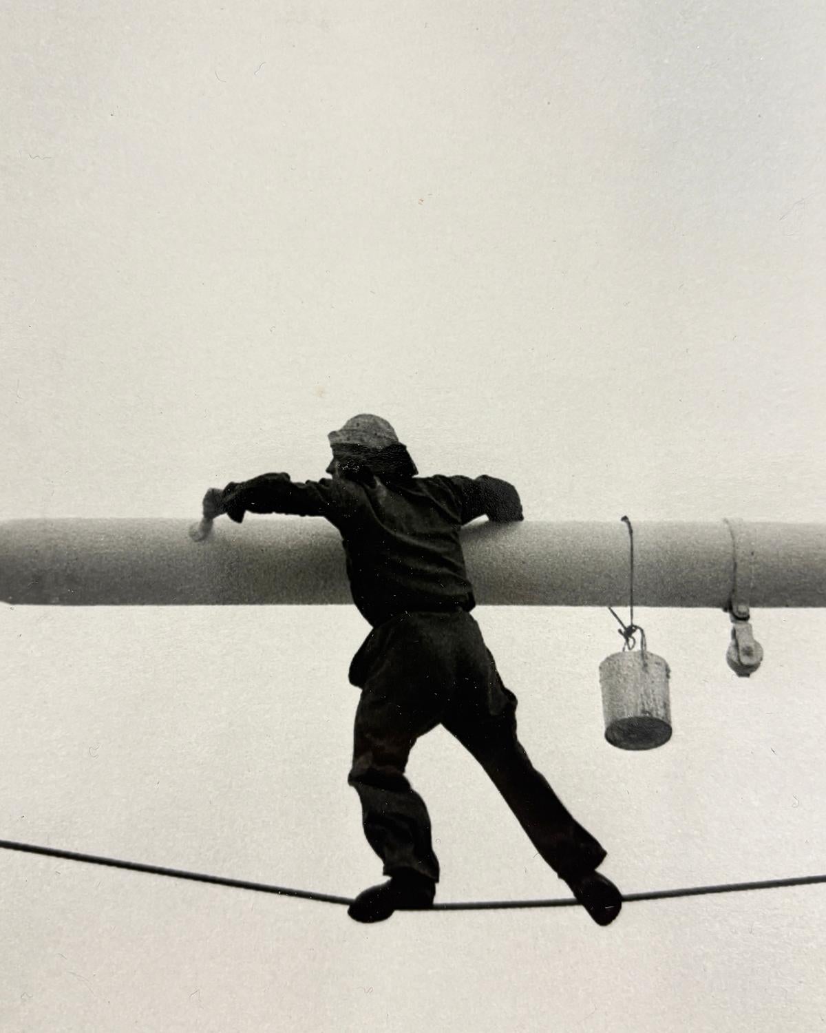 Malerbalken (S/W-Fotografie aus den 1950er Jahren von einem an einem Draht hängenden Mann) (Grau), Black and White Photograph, von Arthur King