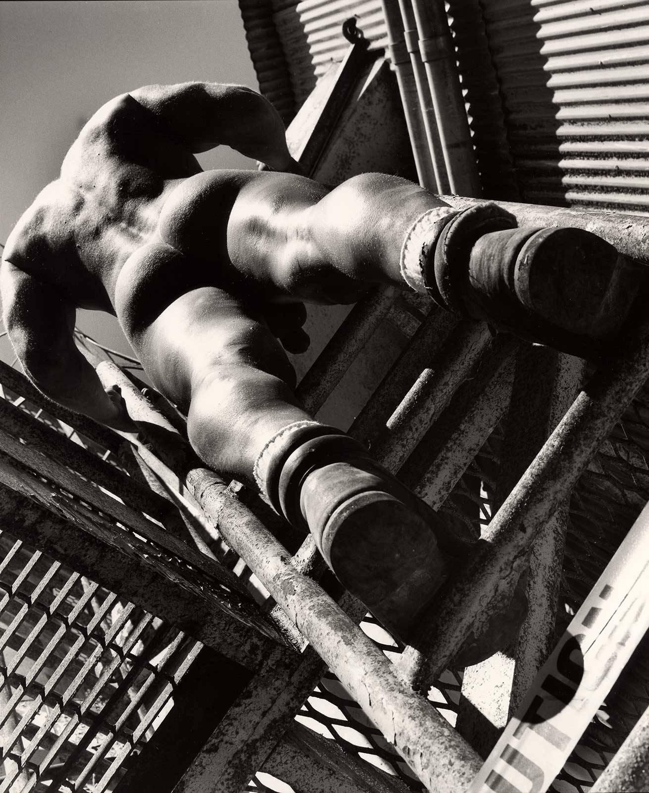 Arthur Tress Figurative Photograph - Caution: Man at Work (Nude construction worker clad only in boots climbs ladder)
