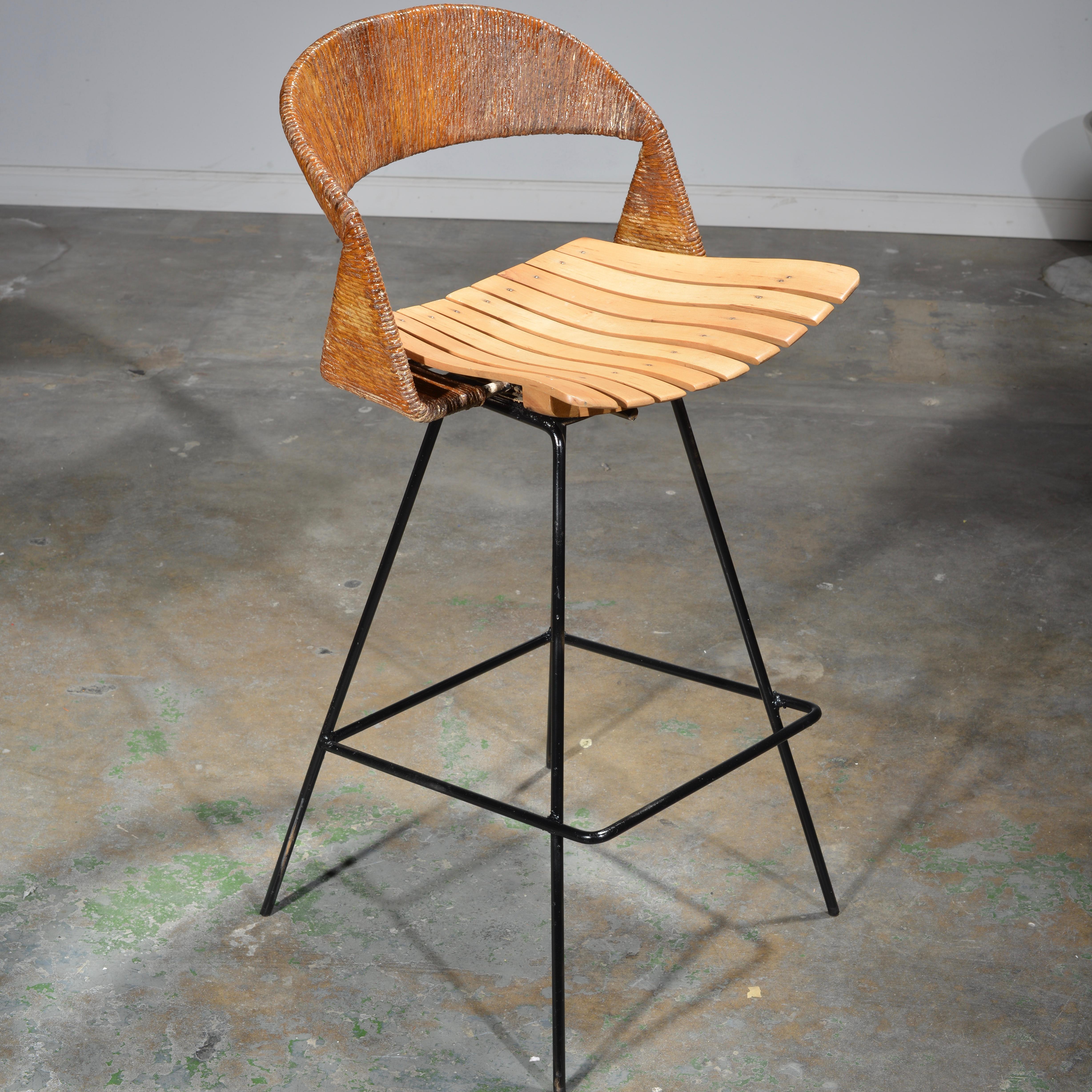 We have 2 of these rare rotating, counter height stools by Arthur Umanoff. These stools are thoughtfully crafted with a steel frame, birch seat, and jute wrapped around the seat back, all materials quite typical for Umanoff’s designs. 

Arthur