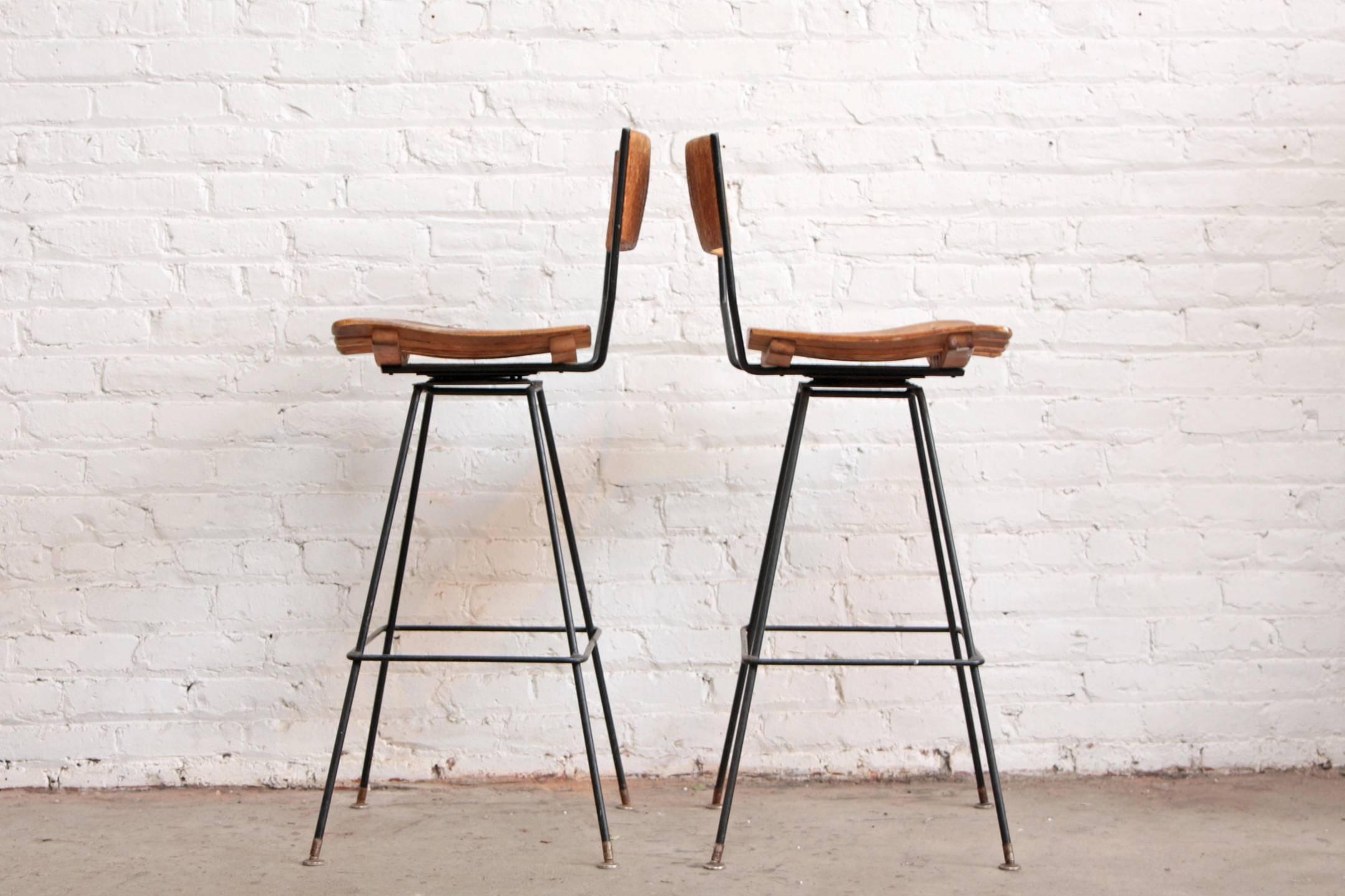 A pair of Arthur Umanoff swivel bar stools. Wrought iron minimalist frames, wood slat seats and papercord backs. 

Measures: Seat height 30
