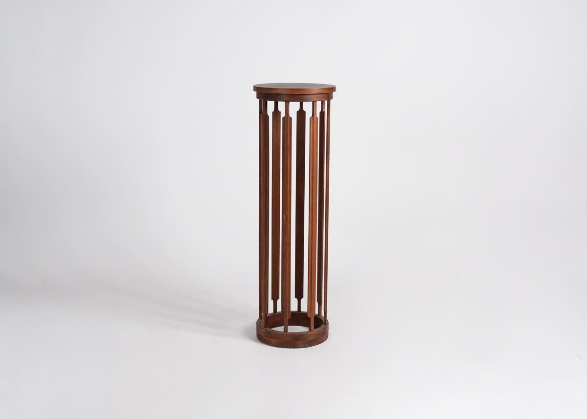 Un élégant support cylindrique pour plantes, fabriqué en bois et reposant sur huit pieds fins et régulièrement espacés.