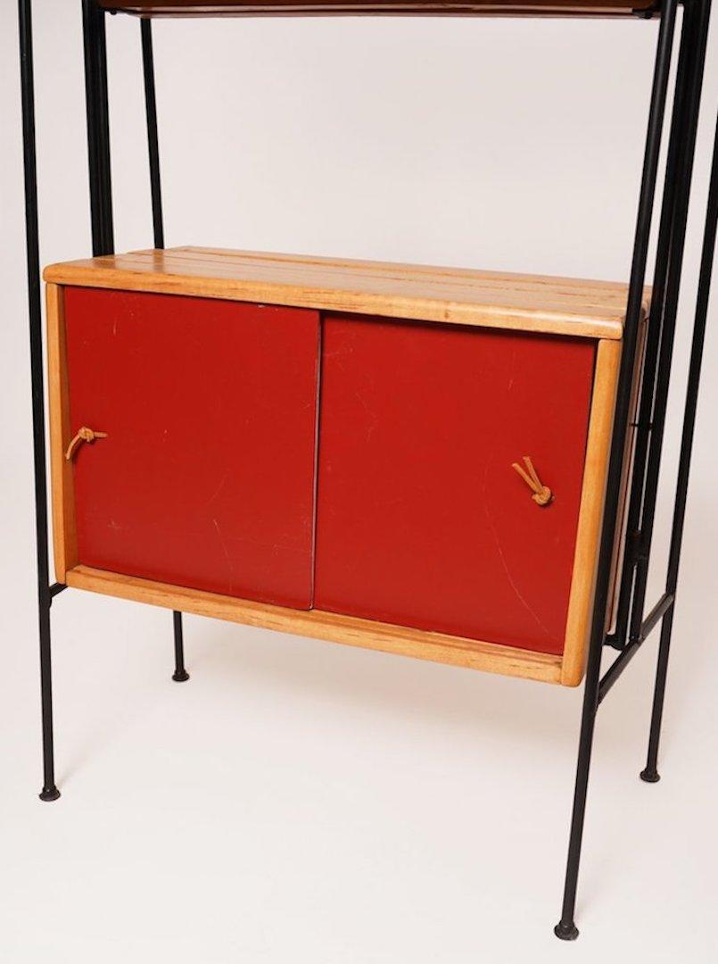 This Arthur Umanoff double-sided room divider shelving unit is both functional and mesmerizing featuring masonite red and citron panel sliding doors with original leather string pulls, slatted wood shelving, natural fiber top and iron frame. This is