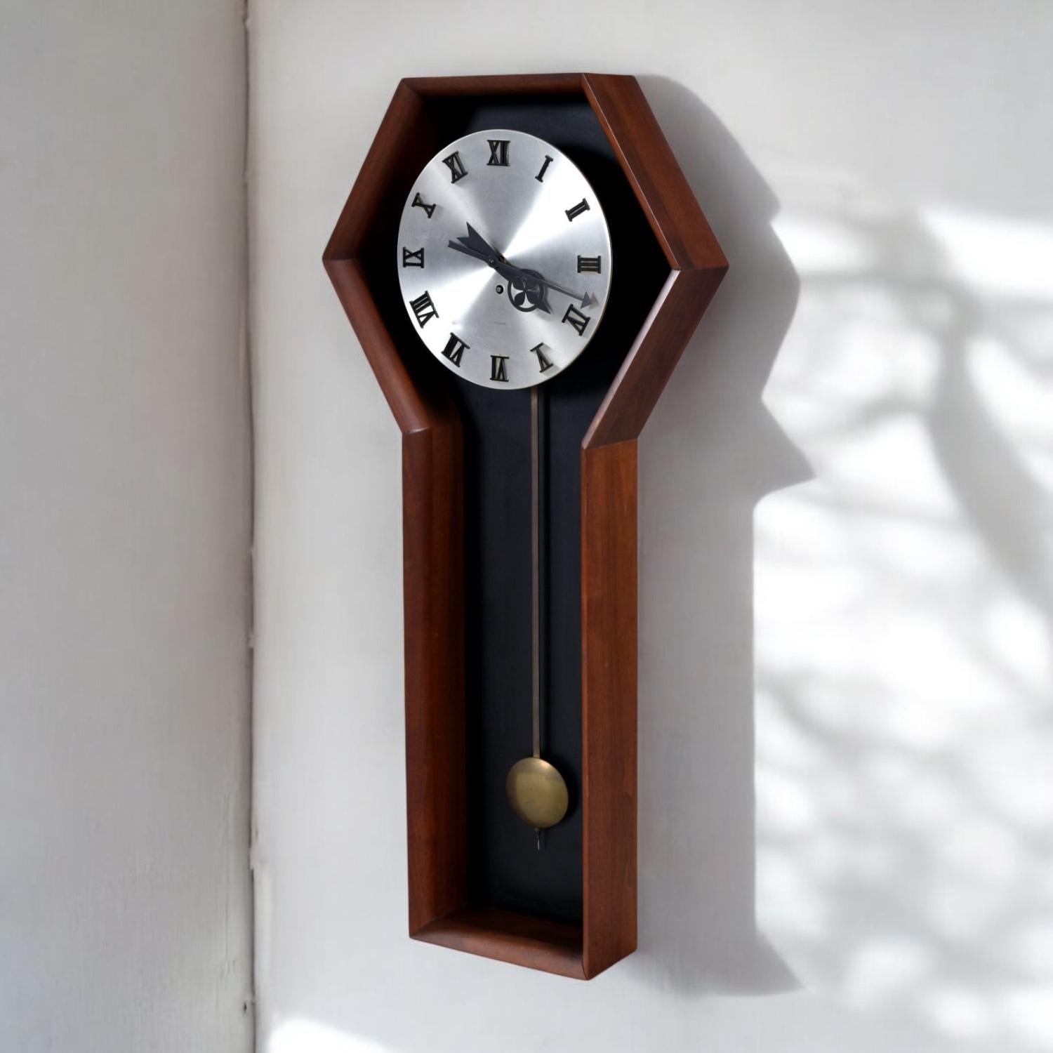Seltene Meridian Pendelwanduhr von Howard Miller. Modell 557, entworfen von Arthur Umanoff für Howard Miller, ca. 1970er Jahre. Das Chassis aus Walnussholz bildet einen schönen Kontrast zu der schwarzen Masonite-Rückwand. Das schlanke Zifferblatt
