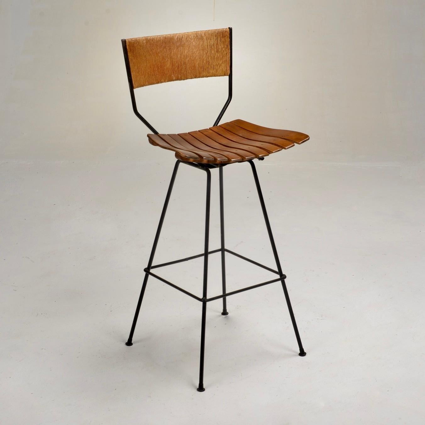 Mid-Century Modern bar stools by American designer Arthur Umanoff. This classic bar stool is versatile and transforms any space. Featuring a wood slat, adjustable swivel seat, a rope wrapped back, and wrought iron legs and structure. Arthur Umanoff