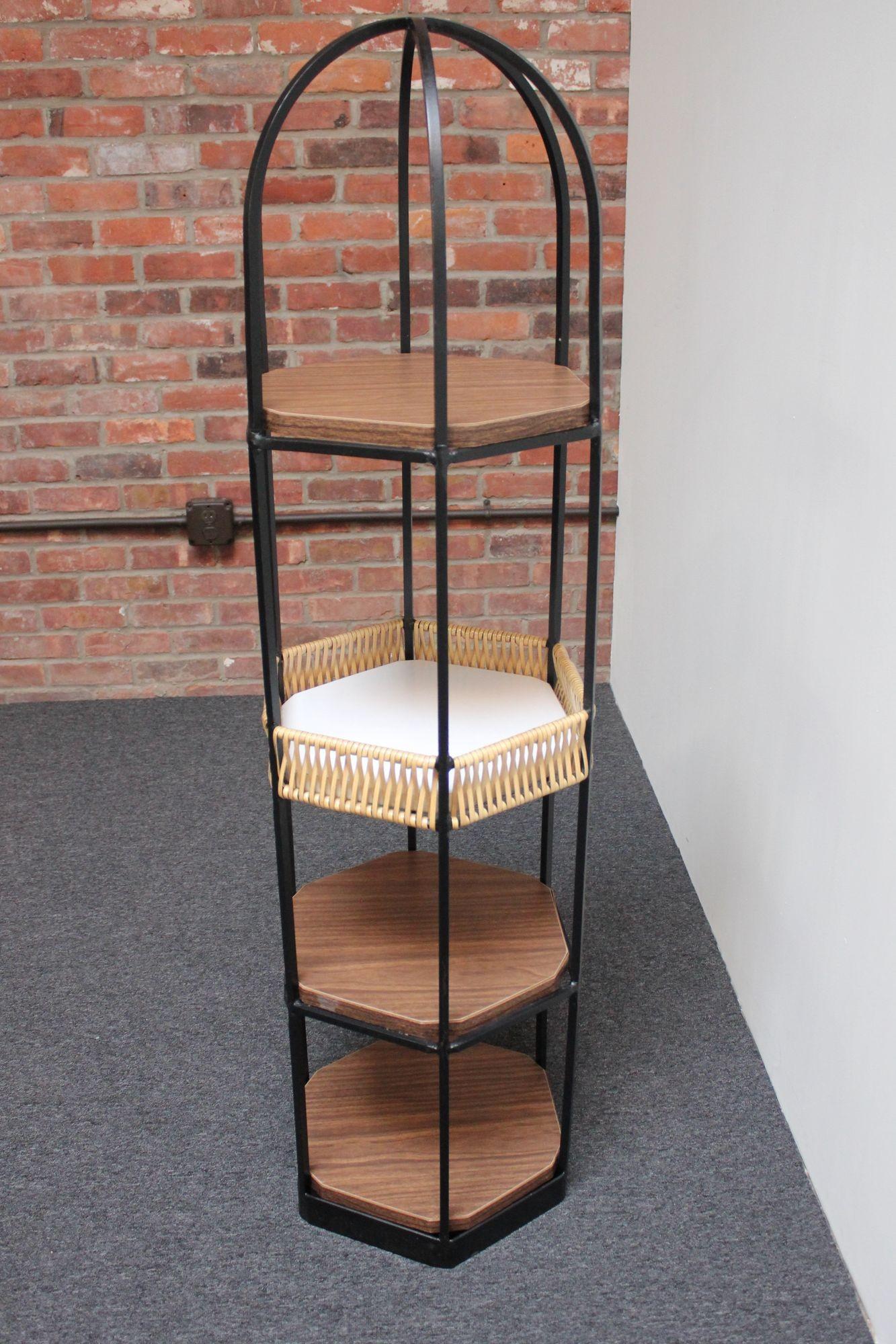 Sculptural wrought iron shelving unit designed by Arthur Umanoff for Shaver Howard.
Unique, graceful form with three hexagonal shelves in faux wood grain laminated pressboard and a rattan basket. Practical, aesthetically pleasing storage/display