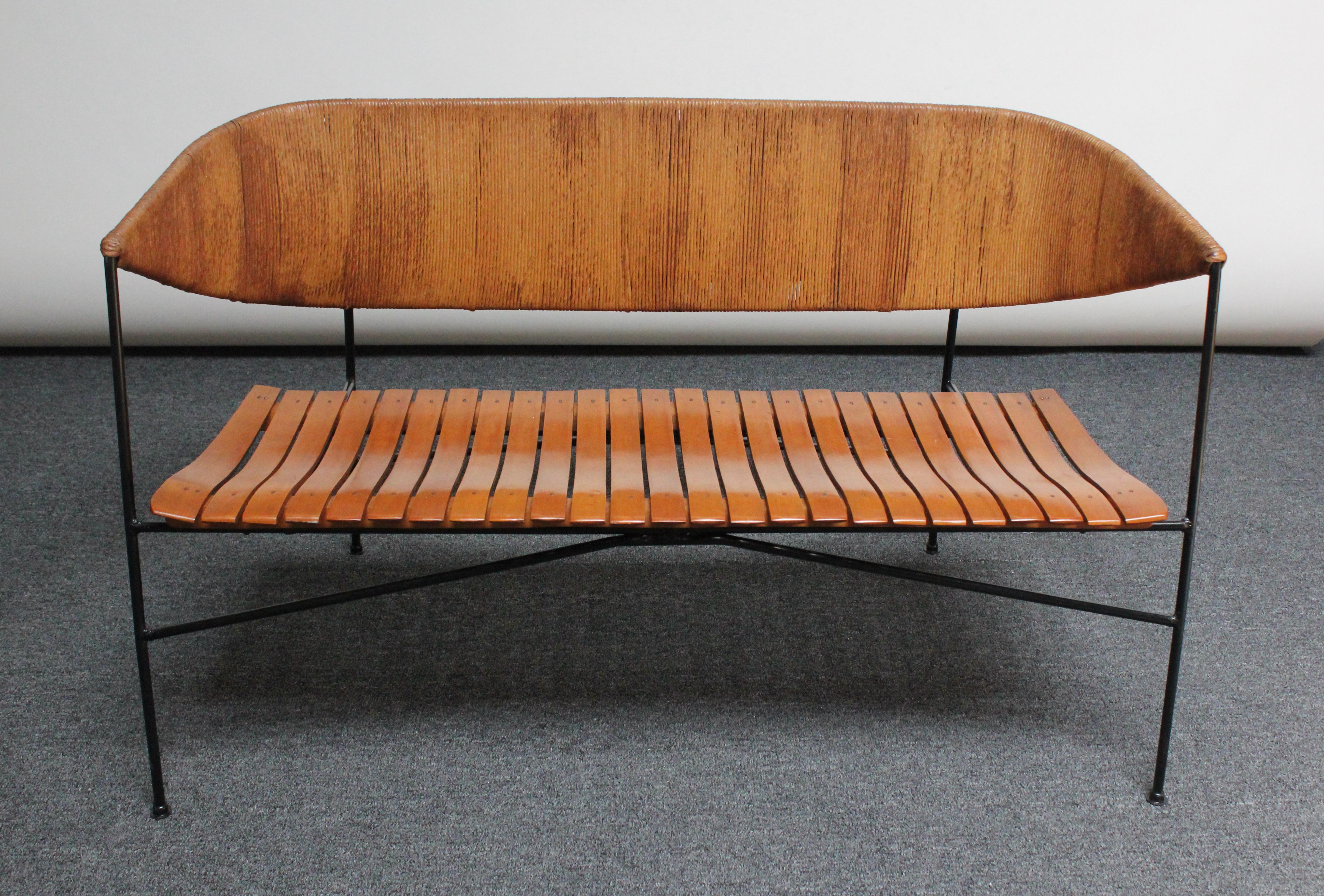 Uncommon Arthur Umanoff for Shaver Howard bench / settee composed of a wrought iron frame with rush back and stained birch-slatted seat. Dramatic, clean lines and modernist form, showing well from all angles. 
Rush is in original condition boasting