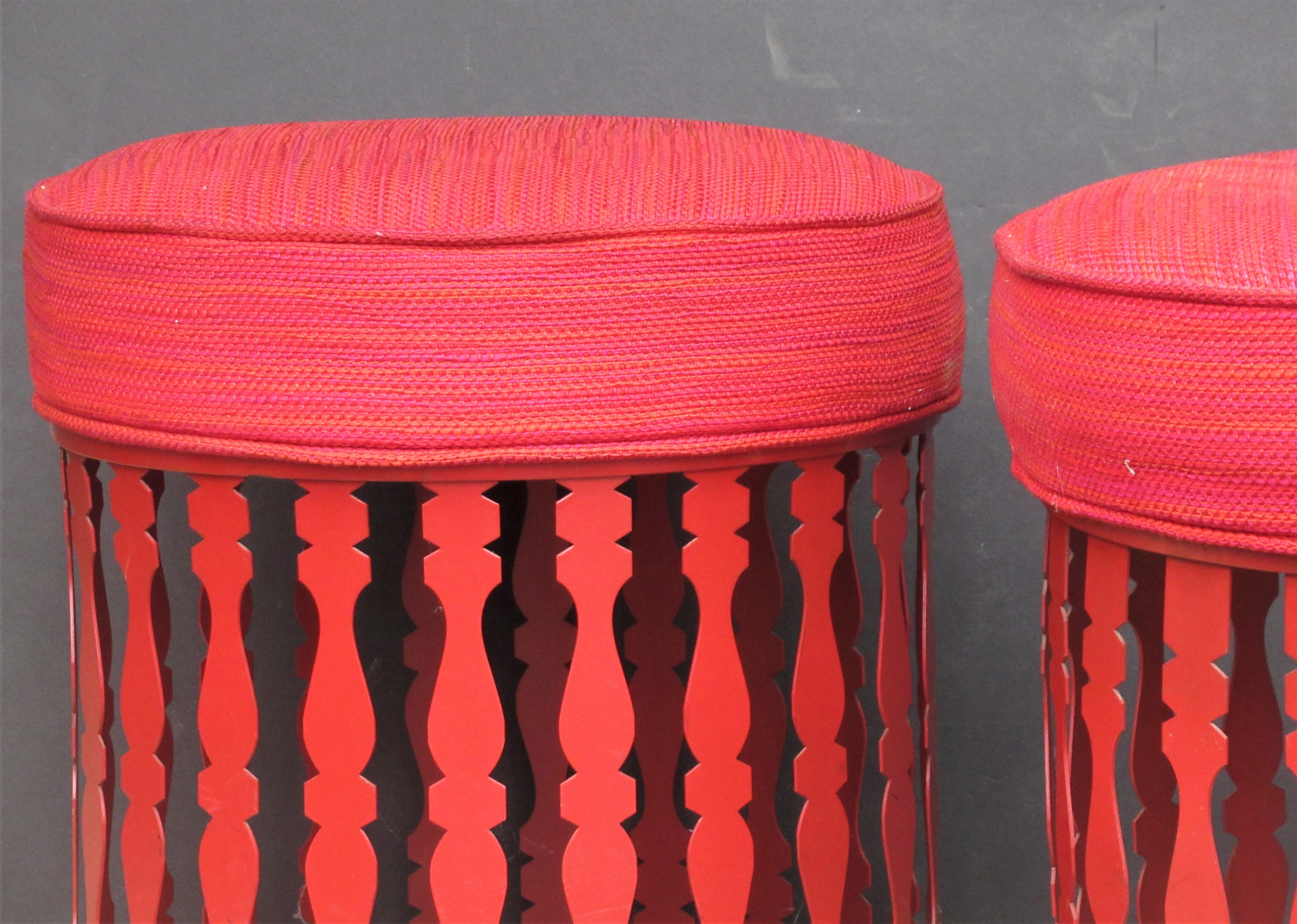 Matching pair of round decorative iron ottomans poufs sitting stools by Arthur Umanoff for Shaver Howard in all original beautiful glowing Chinese red enamel painted surface. The original complimenting colorful textured seat upholstery is very