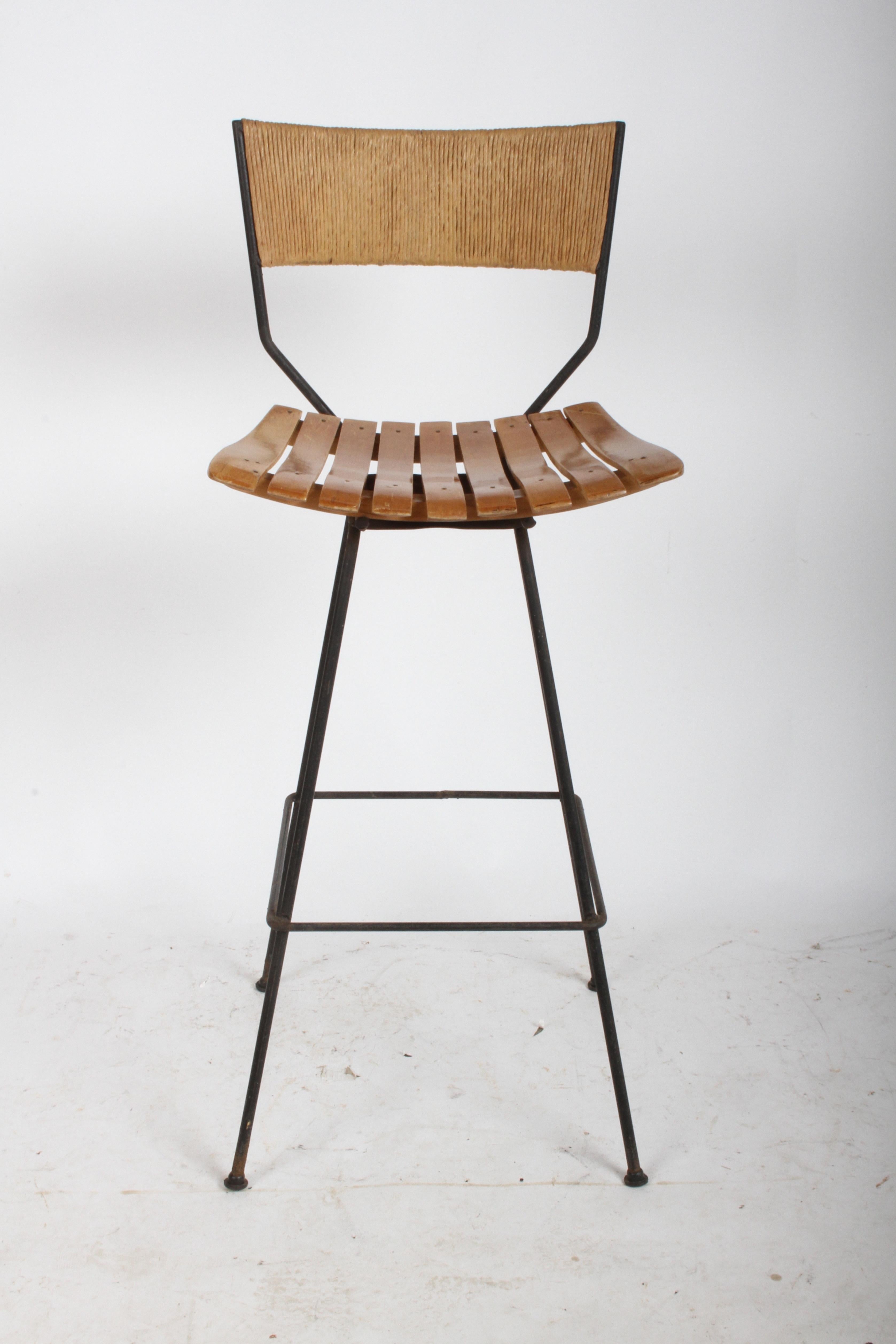 Single Arthur Umanoff swivel bar stool, wood slat seat, iron frame with Danish rush cord wrapped back. If you need another stool to complete your set, here is one that is left unrestored, so you can match. Frame retains original glides, some rust to