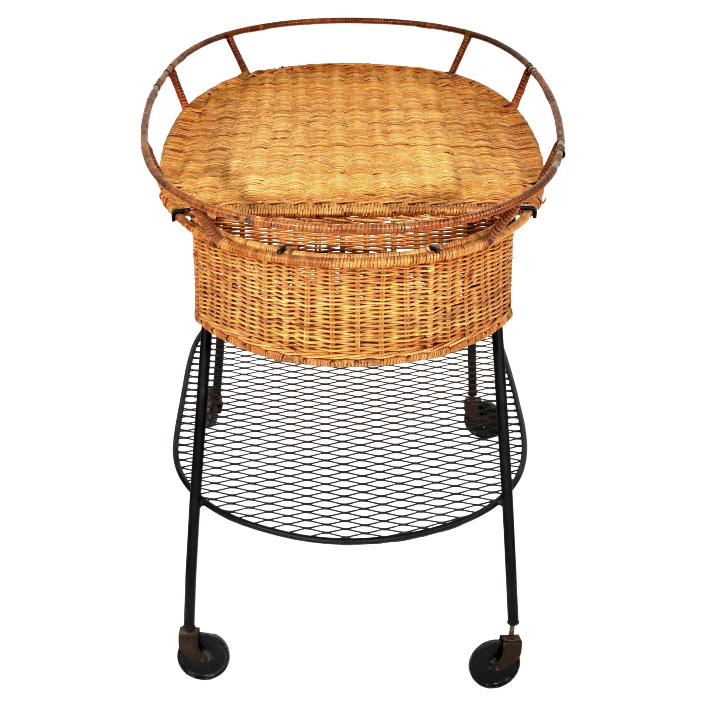Vintage Mid-Century Modern wicker and wrought iron rolling bar cart attributed to Arthur Umanoff. The indoor/outdoor two-tiered serving trolley features a woven rattan top with a removable basket, a black iron lower tier, and a wrought iron frame