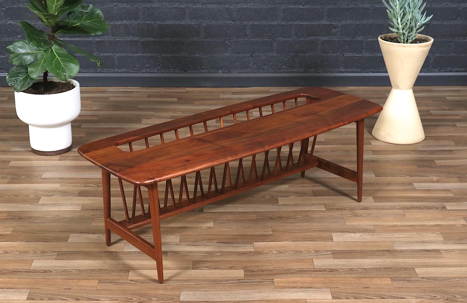 Designed by Arthur Umanoff for Washington Woodcraft, this spindle coffee table perfectly balances functionality and mid-century charm. Crafted with a slatted wood top and spindle magazine rack, it offers a light, airy aesthetic while providing