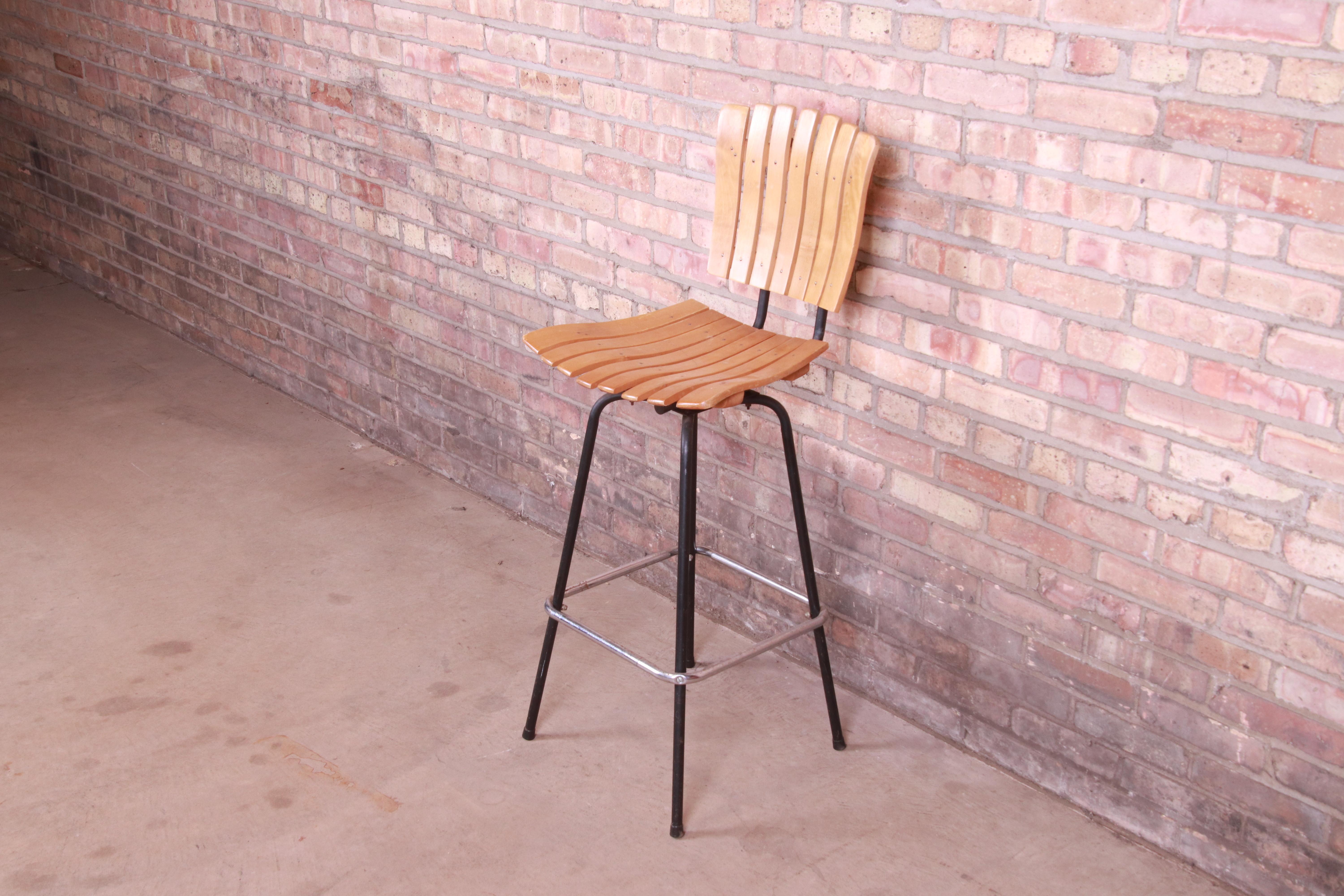 A gorgeous Mid-Century Modern swiveling bar stool

In the Manner of Arthur Umanoff

USA, Circa 1960s

Slatted wood seat and back, with steel frame.

Measures: 17