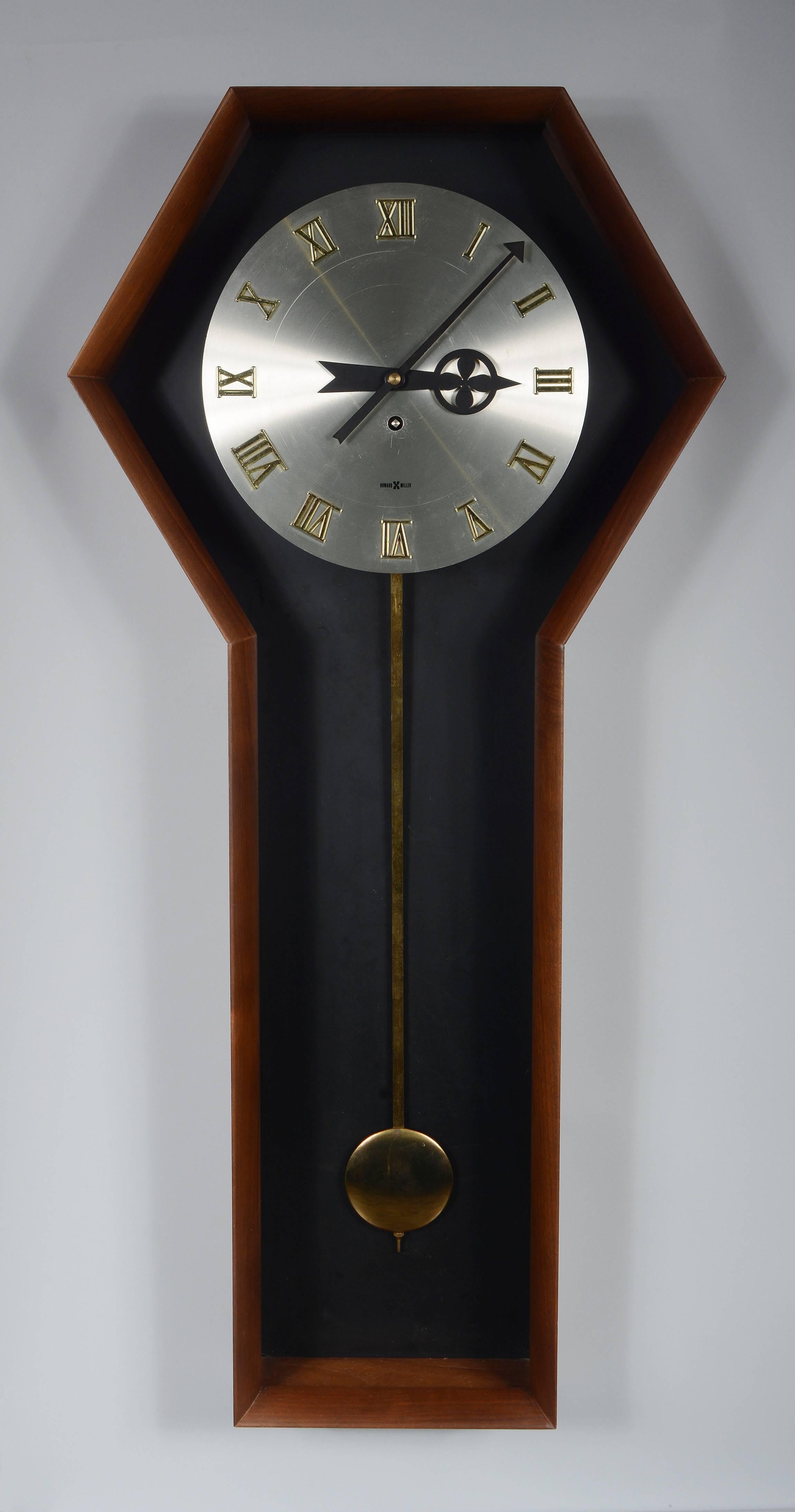 Howard Miller pendulum wall clock designed by Arthur Umanoff. This clock has a walnut case with a floating aluminum face. The clock has an eight day movement. It runs and keeps time.