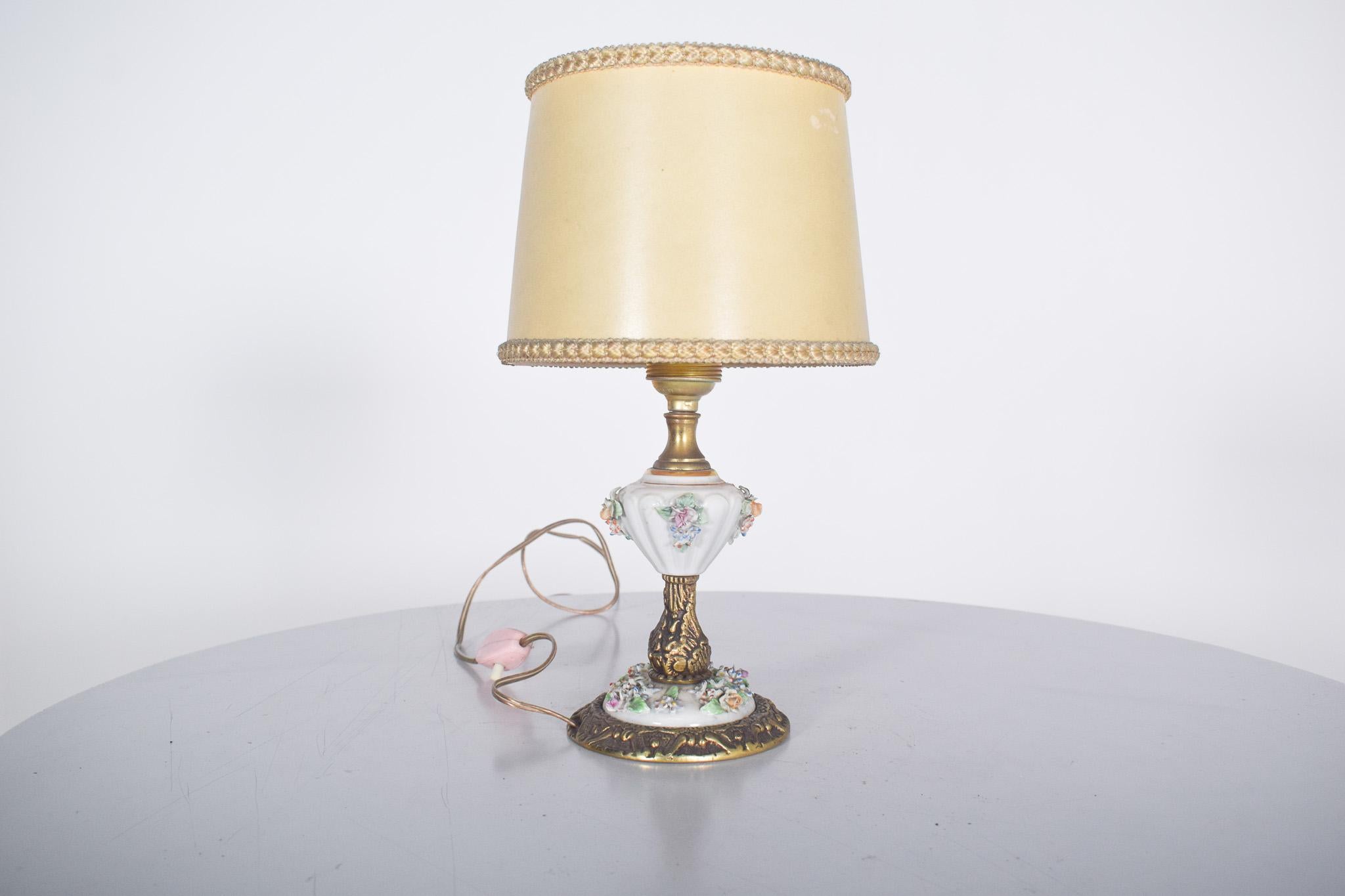 Lámpara de sobremesa Artibus de bronce y porcelana. Elegante pantalla de bronce y metal, con base y cuerpo ricamente decorados. La estructura principal combina metal dorado con detalles de porcelana blanca tallada en relieve, decorada con delicadas