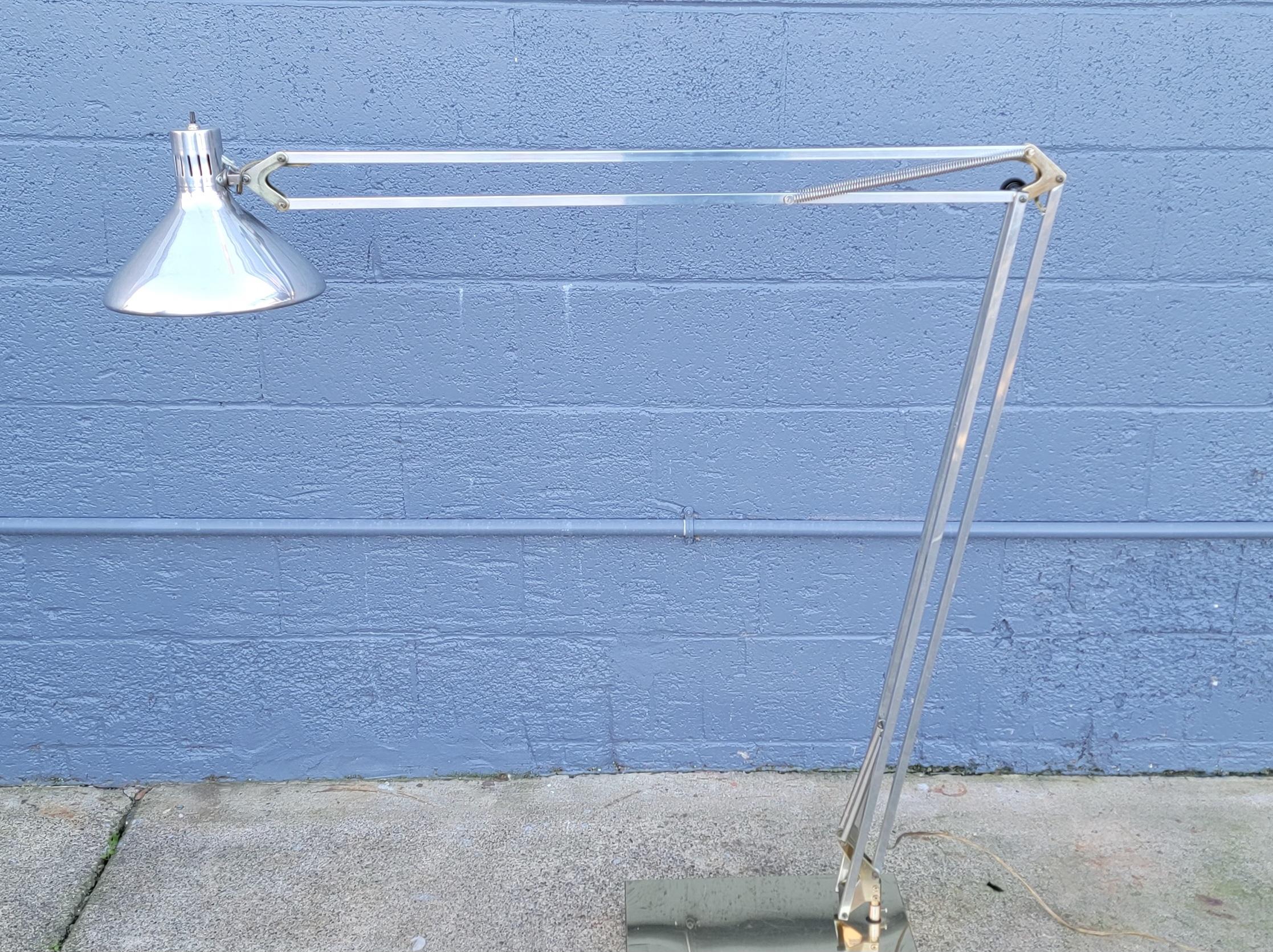 Adjustable floor or arc lamp made of aluminum with brass accents and brass base. Measurements of lamp vary depending on positioning. Measure: height ranges between 46-80 inches. Base measures 8.5 inches by 16 inches. Over-all very good condition