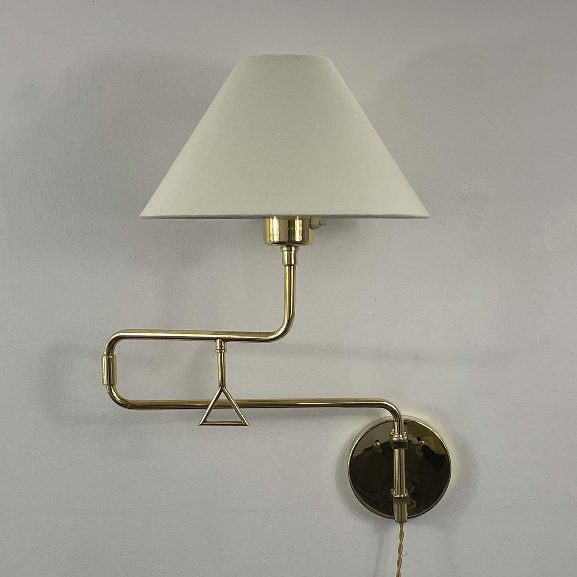 This elegant wall light was designed and manufactured in Sweden by Armatur Hantverk Tibro in the 1950s to 1960s. It features an articulating brass lamp arm and off-white linen lampshade. The light has been rewired with new fabric cord. The shade is