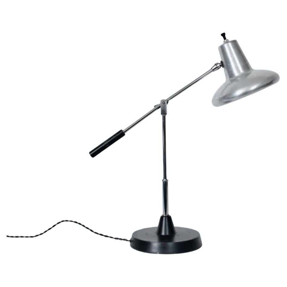 Lampada da scrivania regolabile con paralume in alluminio e base e braccio smaltati di nero. Il paralume in alluminio con presa a sfera, il braccio e la colonna a sbalzo in cromo, la maniglia in smalto nero e la base circolare in metallo. Presa