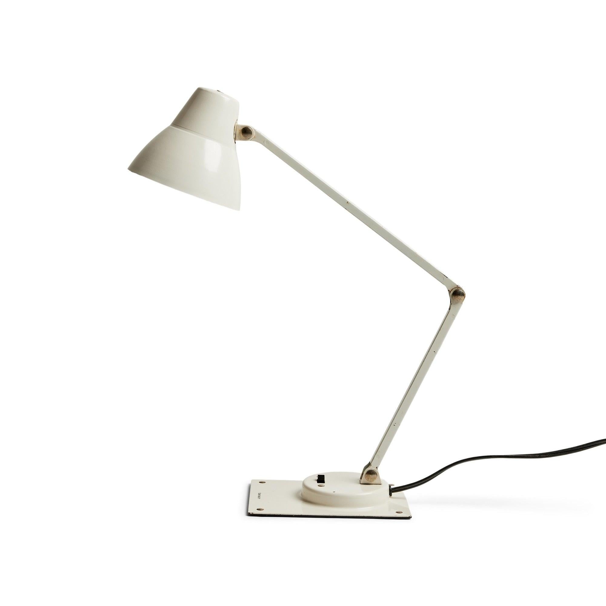 A petite white metal desk lamp with an adjustable arm and shade and a power switch located on its base.