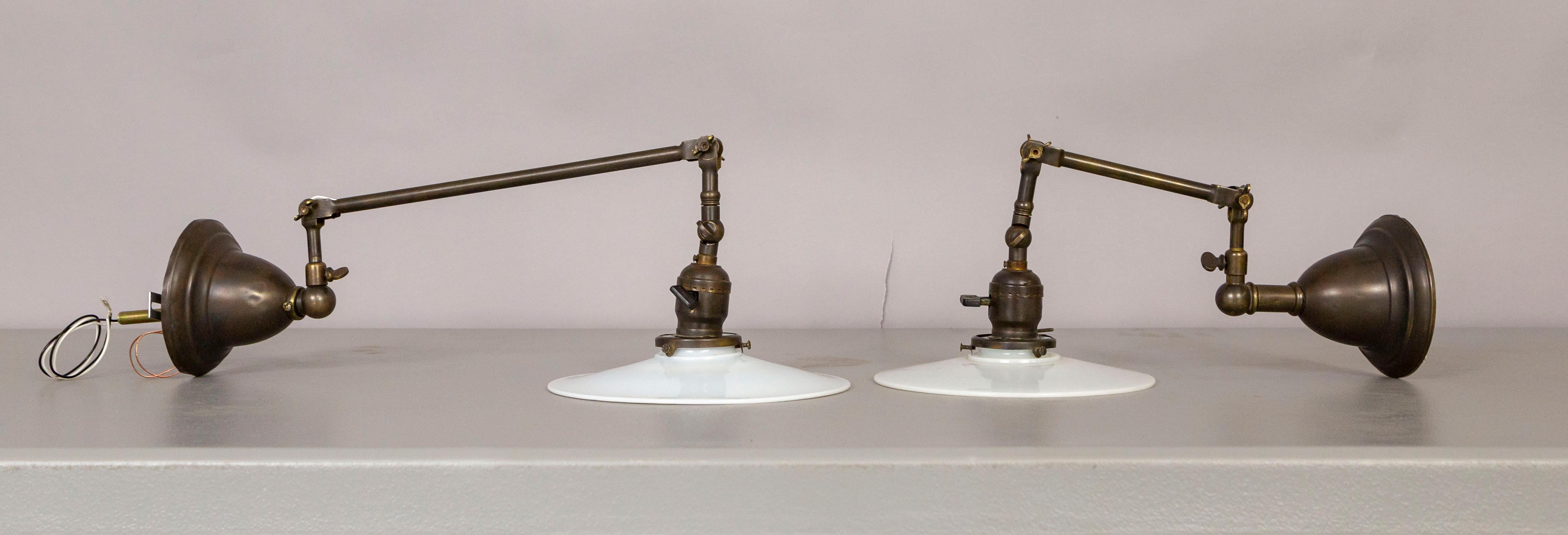 A pair of brass wall sconces with an oil-rubbed bronze finish from the late 1800s, originally gas, now electrified. They articulate in multiple places and make a perfect task light. With milk glass, disk shades, and attractive knob and screw