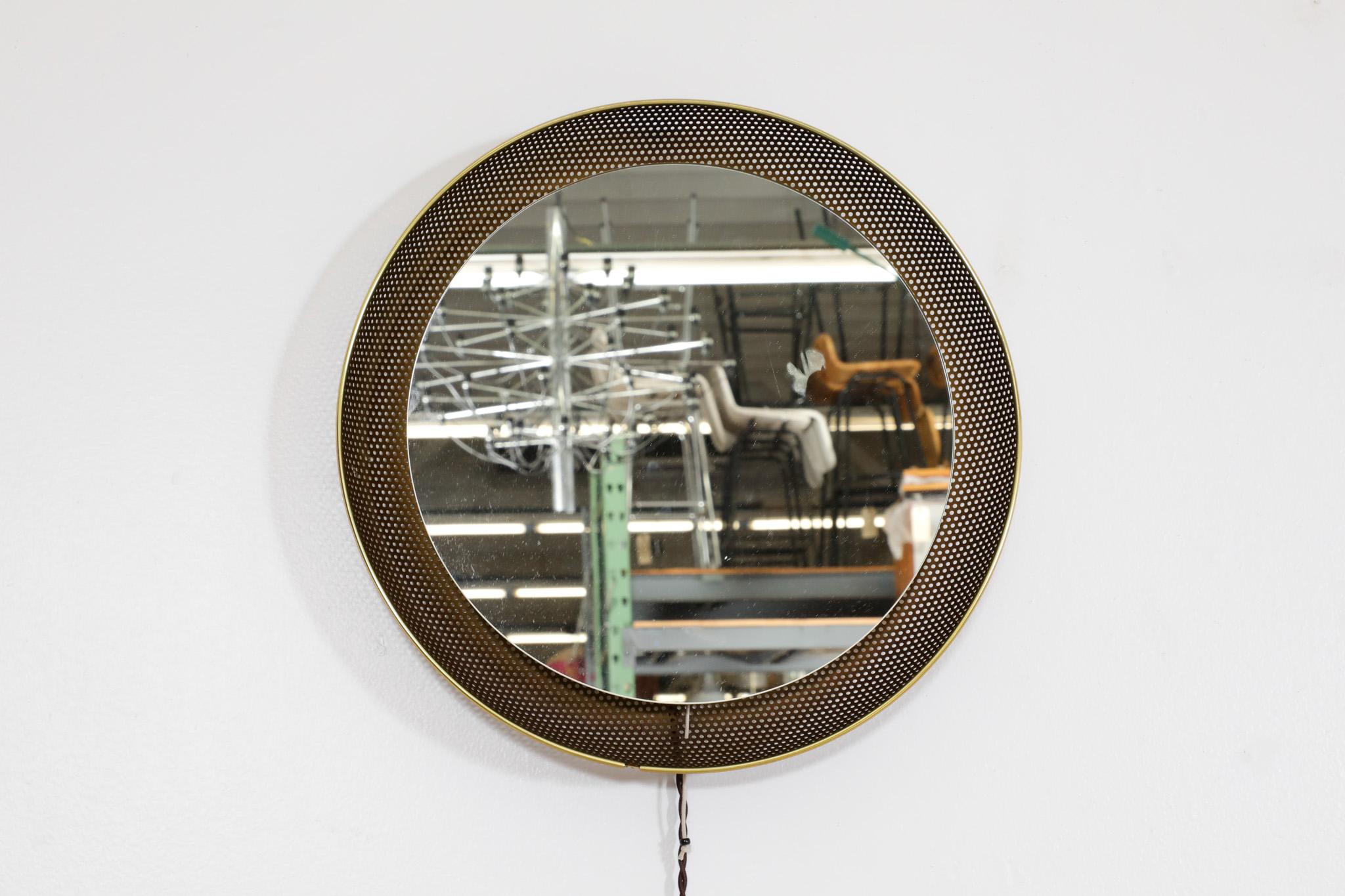Mathieu Mategot inspired back lit mirror with gold toned perforated metal frame, brass trim and pull string switch. In original condition with normal wear for its age and use. Mirror diameter is 13.75