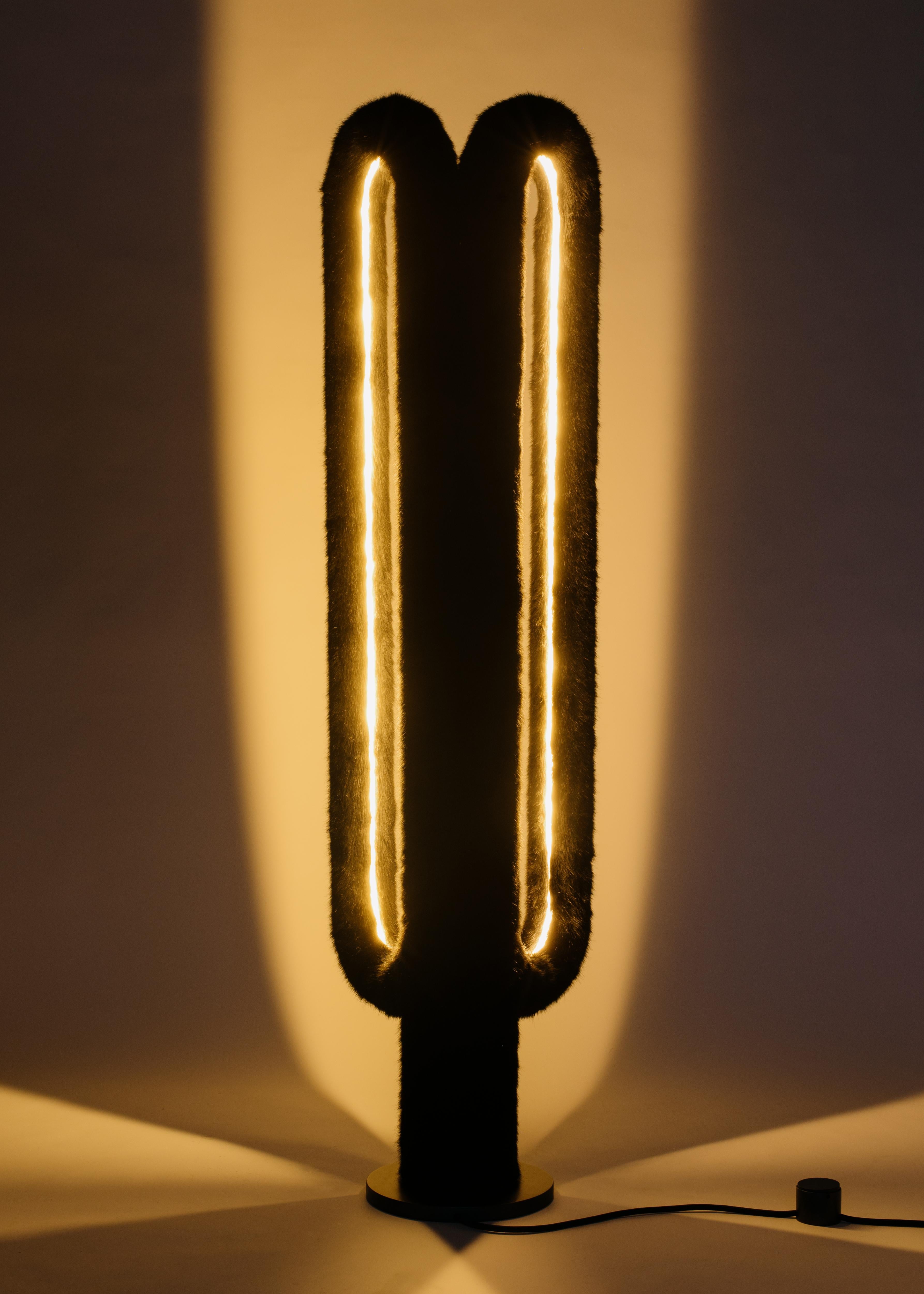 The Artiodactyl Floor Lamp features two standing cylindrical loops of illuminated fur. They glow from the inside of their contours, creating twin pockets of light that accentuate their symmetry and ricochet throughout a room. The lamp is inspired by