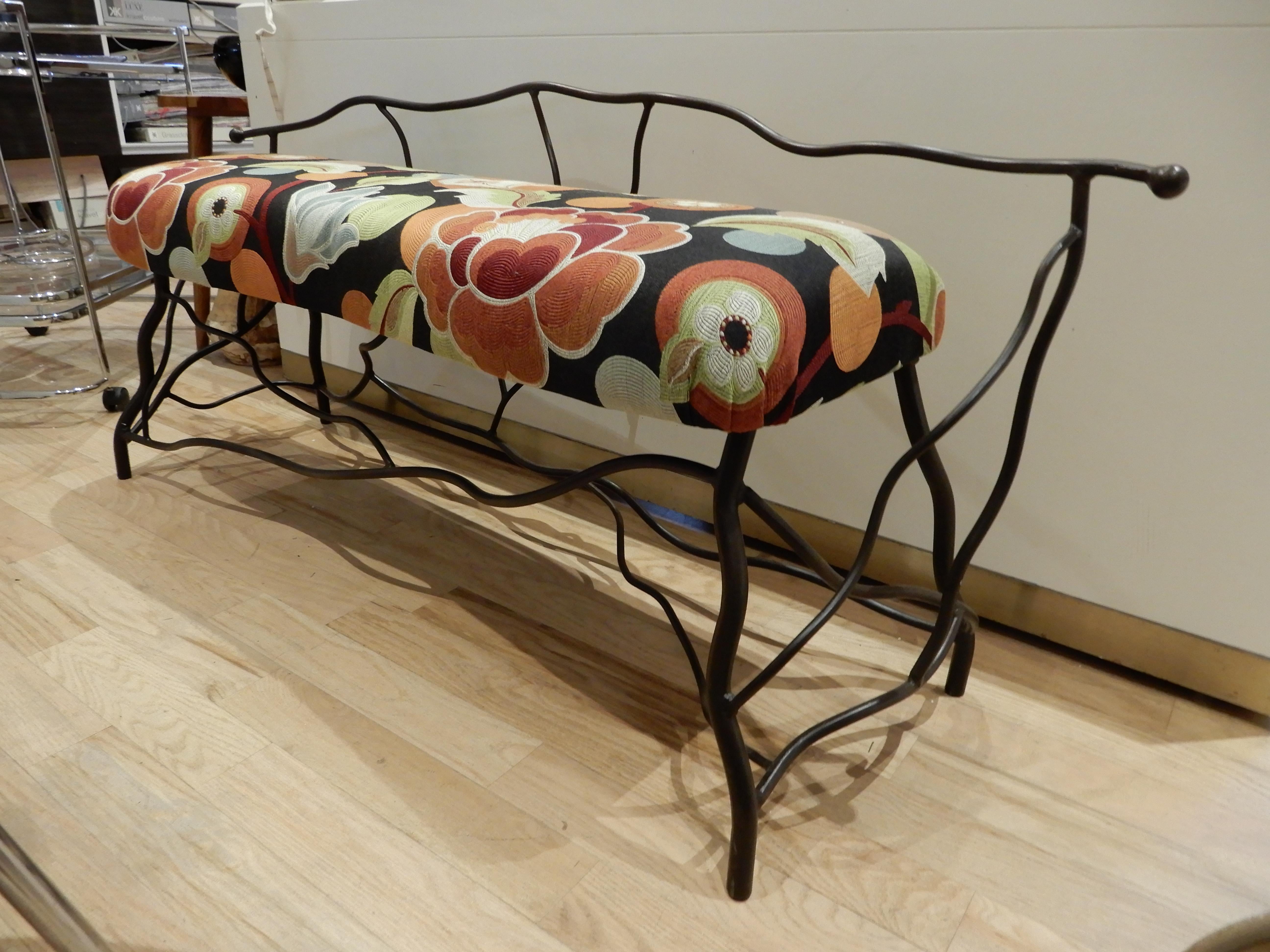 A Giacometti style artisan crafted iron bench. There are two available each priced separately, upholstered with a colorful and graphic botanical textured fabric.