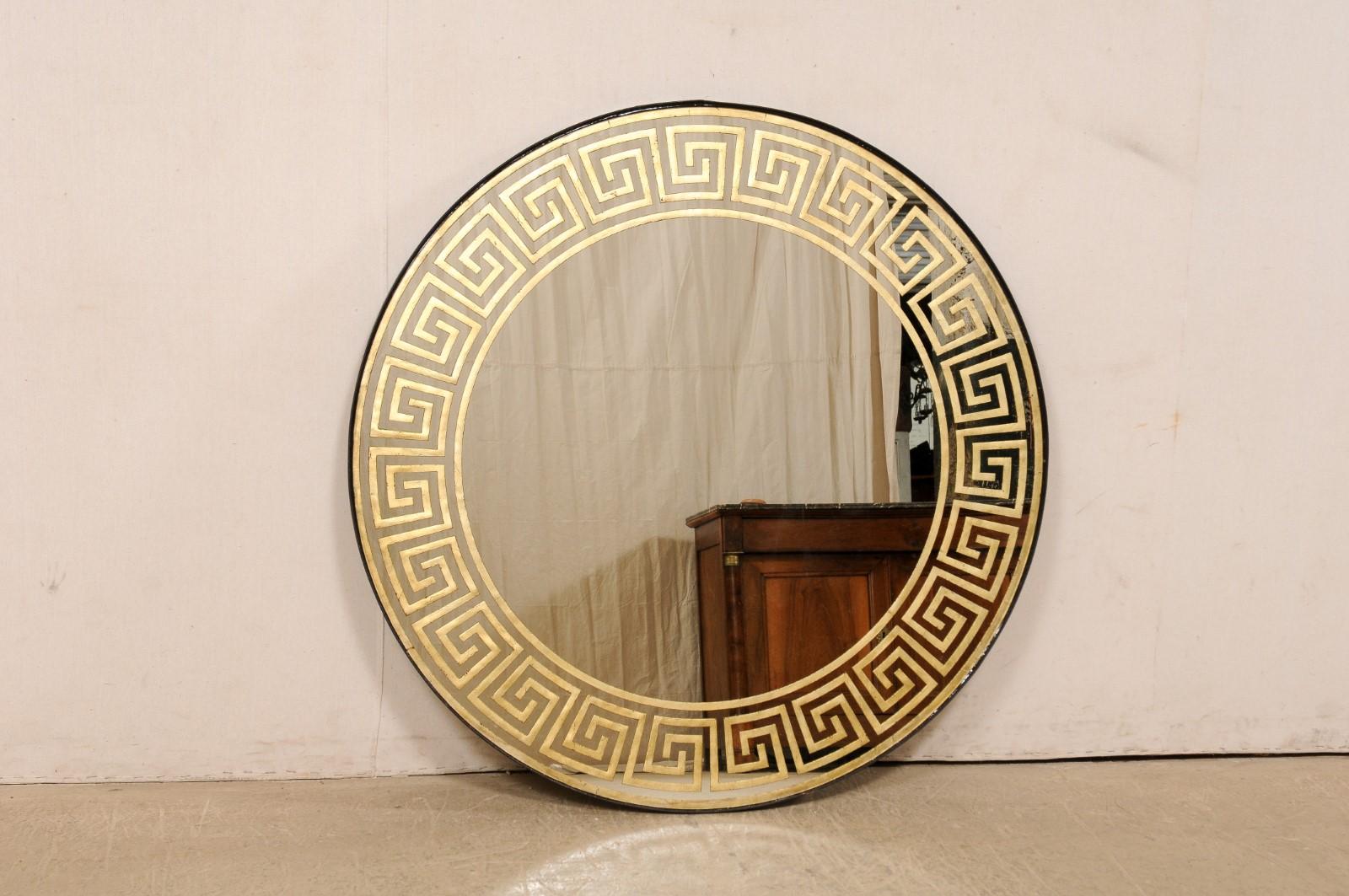 An artisan crafted round mirror with gold églomisé Greek key motif. This nicely sized and round-shaped mirror, with a diameter of approximately 4 feet, has been artisan-crafted with a gold tone églomisé Greek key decorative perimeter banding, and a
