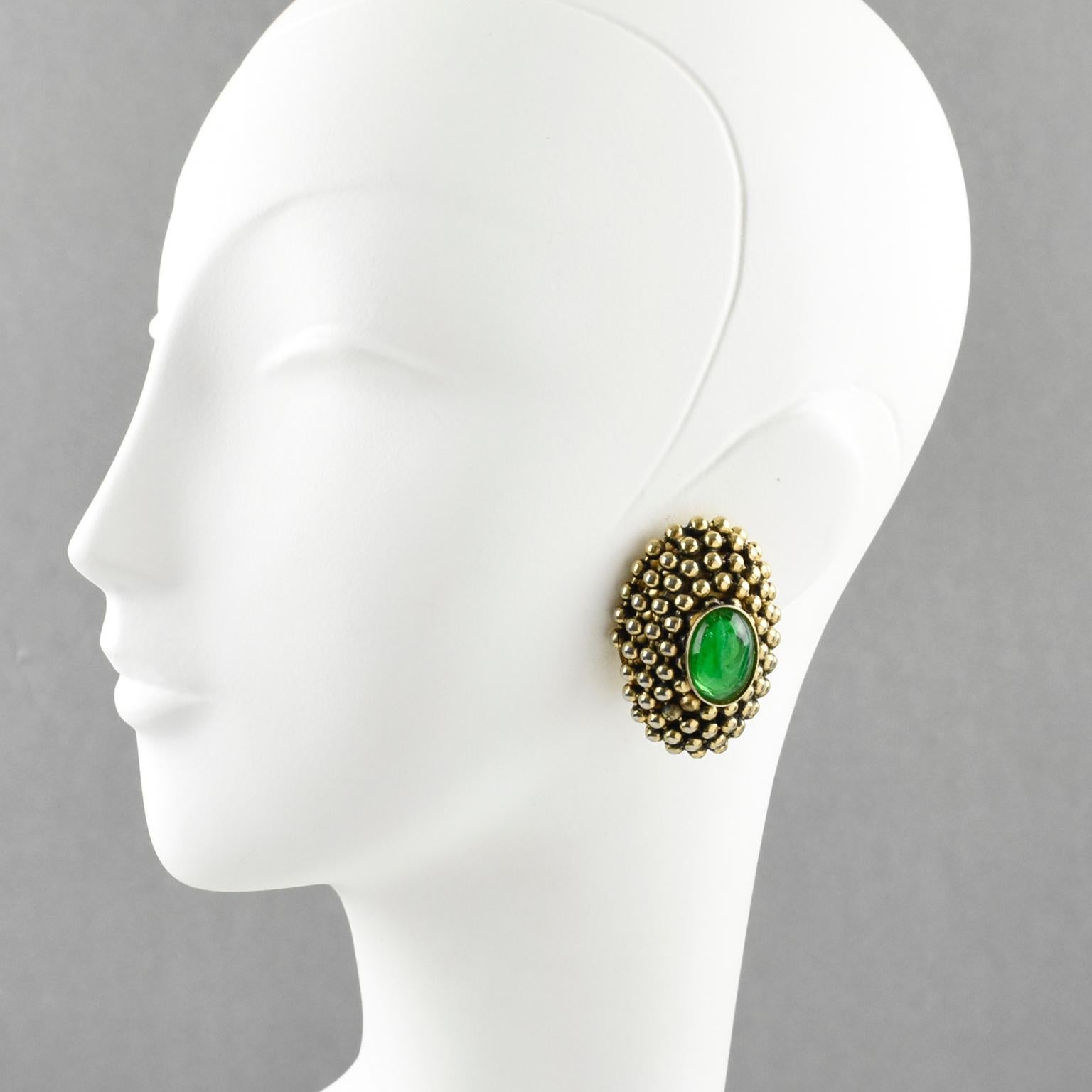 Charming French artisan designer clip-on earrings. The large ovoid dimensional shape is reminiscent of Dominique Aurientis' work. Gilt metal all textured and carved in caviar seeds design, topped with Gripoix emerald green poured glass cabochon. No