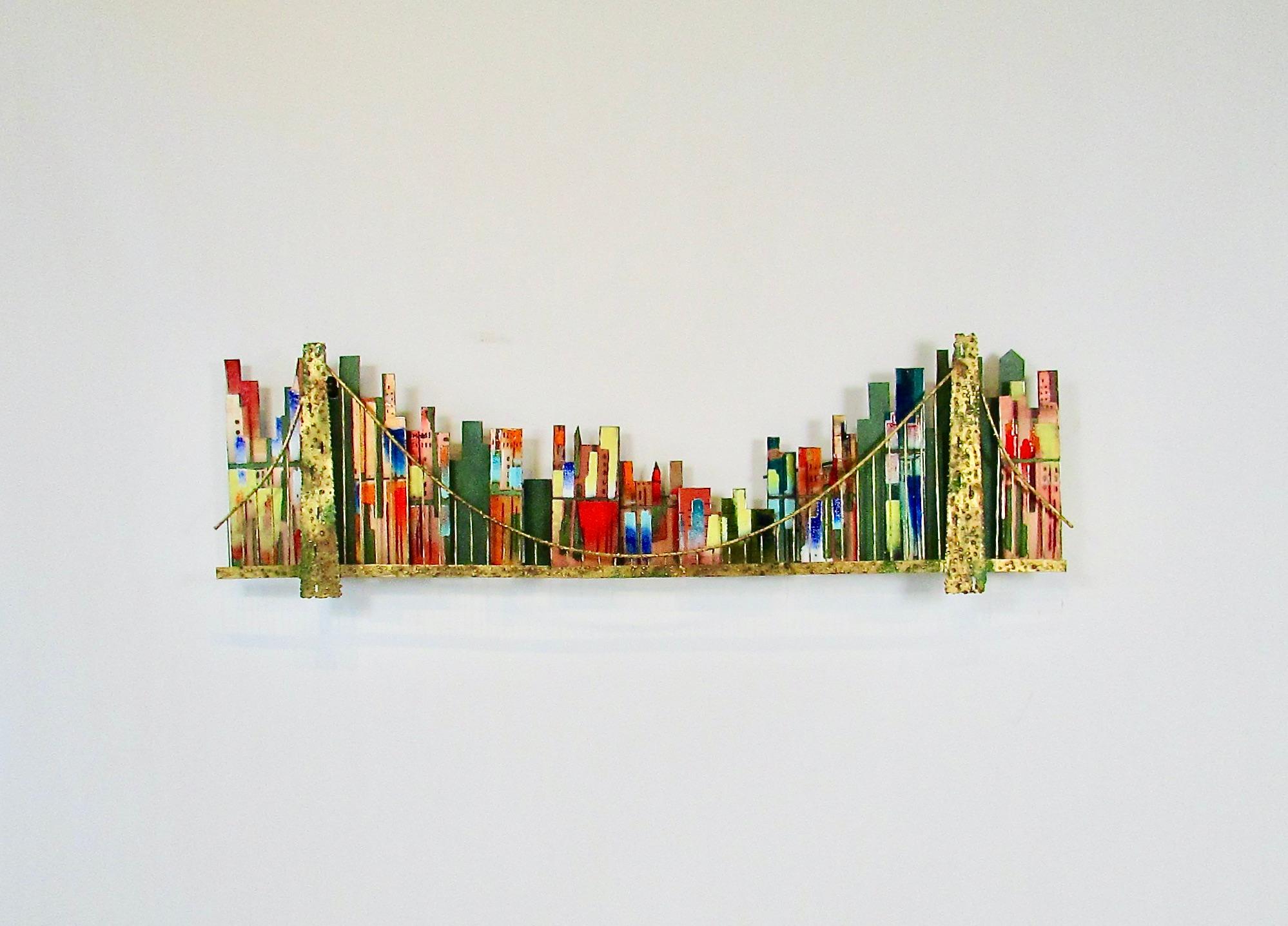 Grande e precoce scultura da parete Artisan House. Molteplici forme di edifici in rame smaltate con colori brillanti  attaccato a una forma in acciaio e ottone che raffigura un paesaggio urbano all'ombra di un'isola.  un ponte . Ci sono alcune