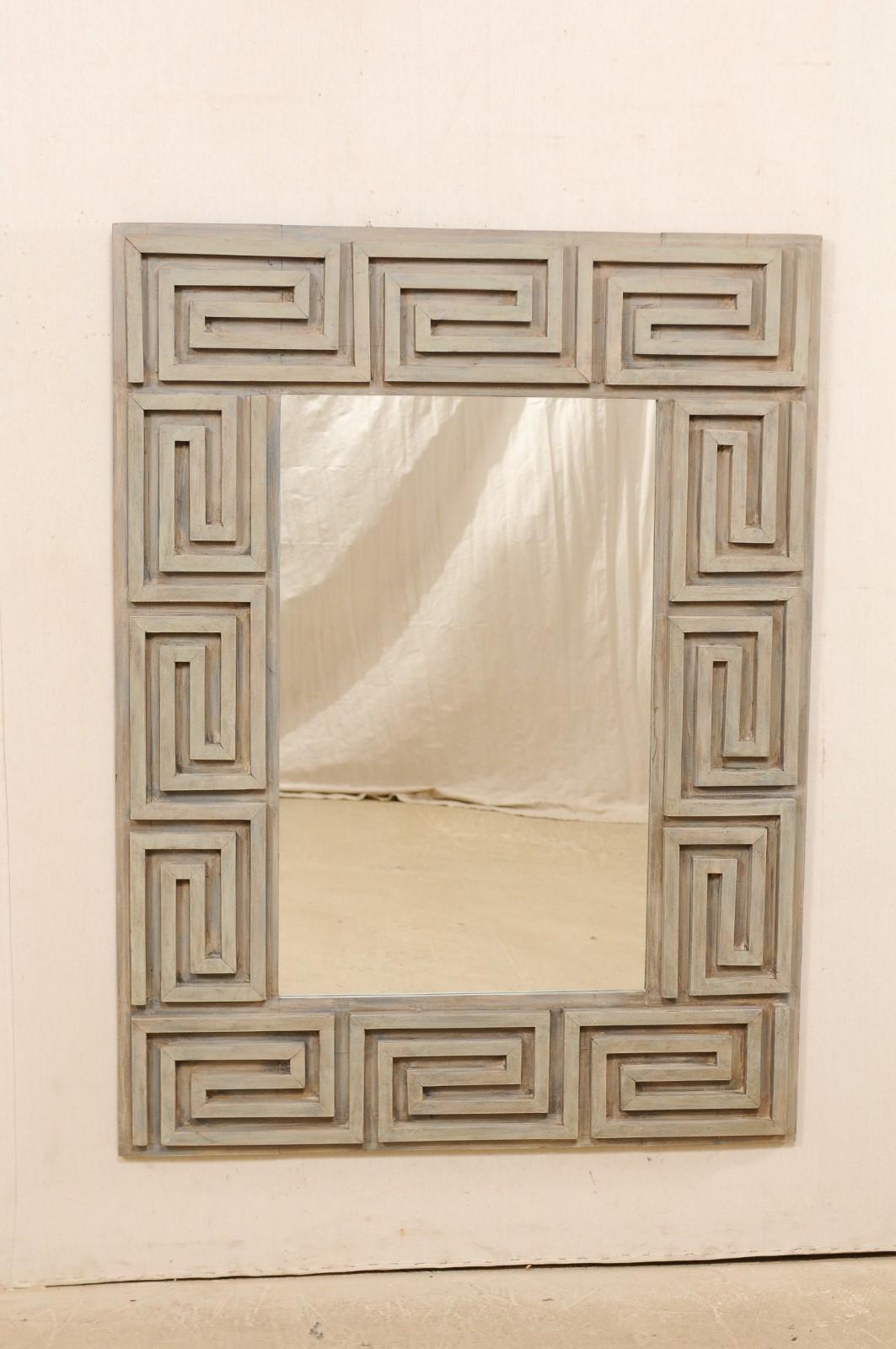 An artisan made mirror with Greek key carved motif surround from old, reclaimed wood. This custom mirror features a raised wooden pattern design of repeating Greek key motif adorning the rectangular-shaped surround. The clear center glass is