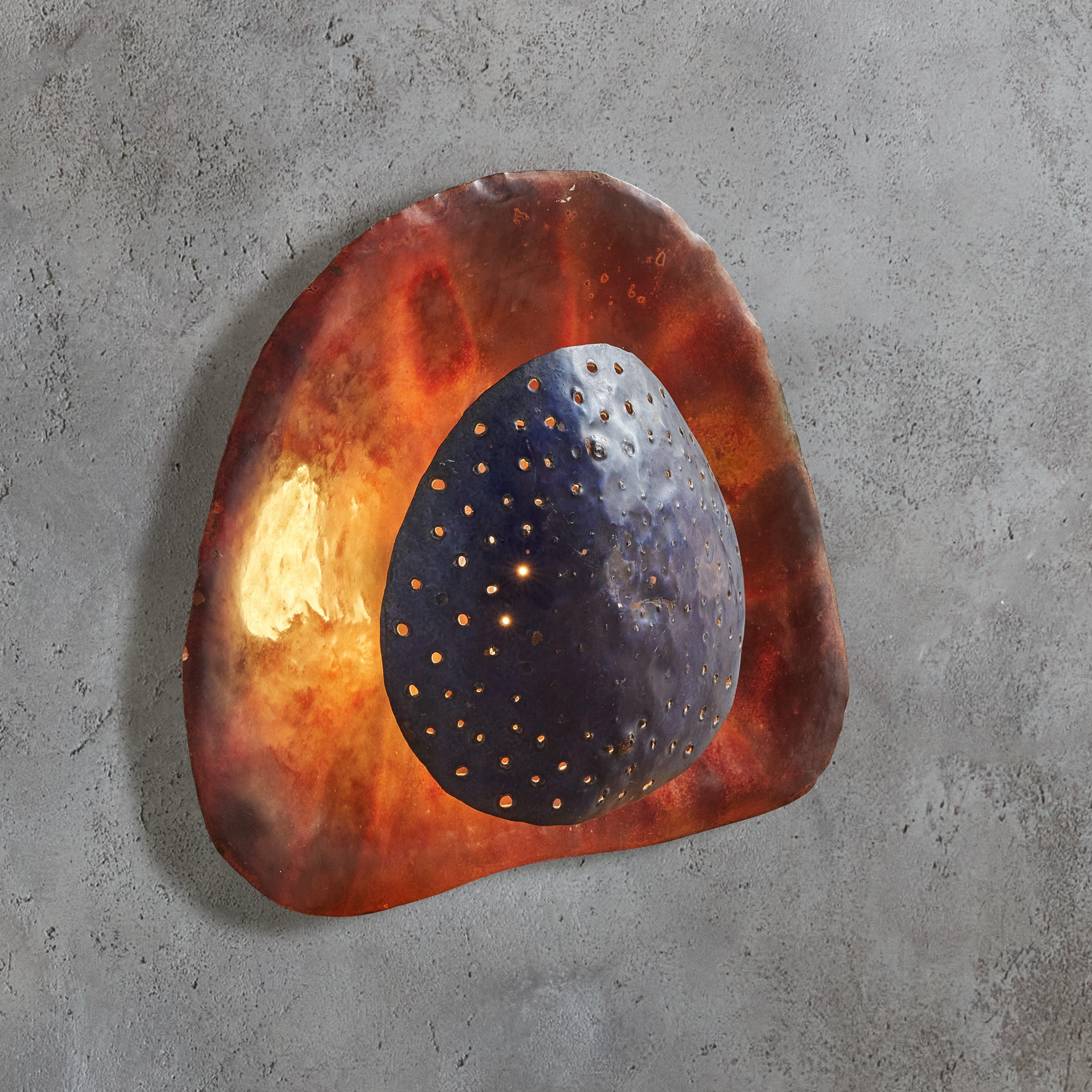 A rare French artisan made metal sconce from the 1950s. The sculptural, organic modern silhouette is composed of two layered patinated metal discs with delicate holes and rich glazing in deep, earthy hues. When lit, shades of olive green, plum, and