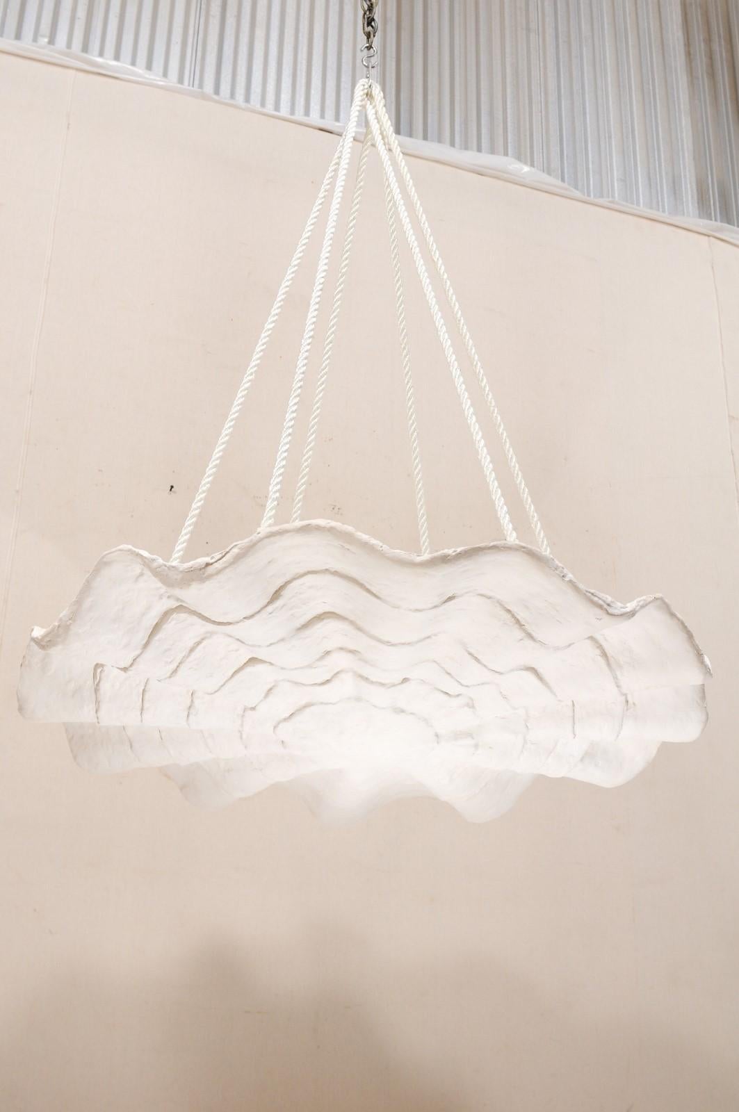 This artisan-made hanging modern light fixture, inspired by midcentury designs, has an overall convex and rounded shape, with undulating waves and concentric ring textures adorning it's downward-facing facade. This hand-crafted plaster light