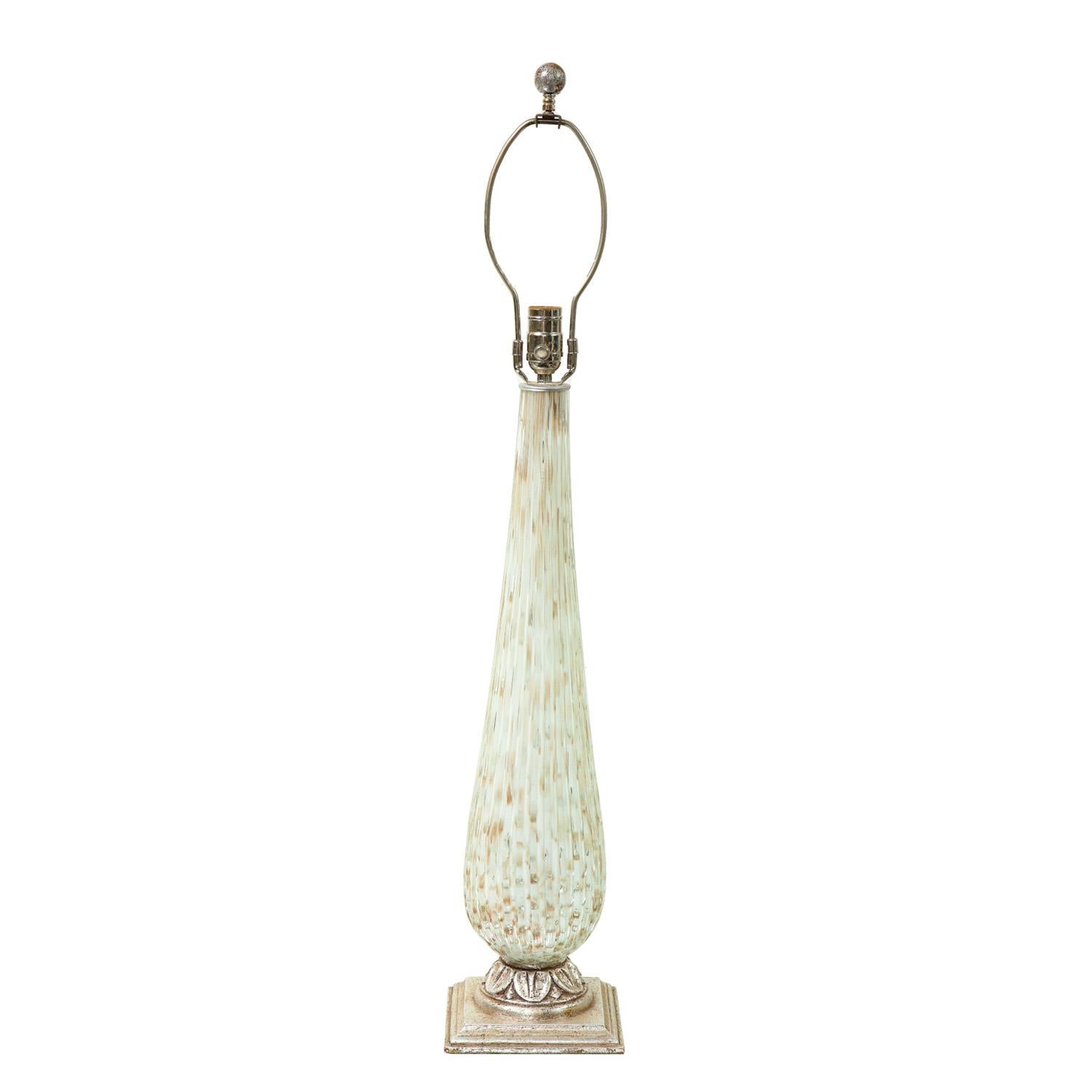 Lampe de table en verre de Murano sommerso transparent et blanc, nervuré, avec inclusions de bullicante et de feuilles d'or. Base en bois sculpté et fleuron en forme de boule, finition en feuille d'argent vieilli. A la manière de Barovier & Tosso, 