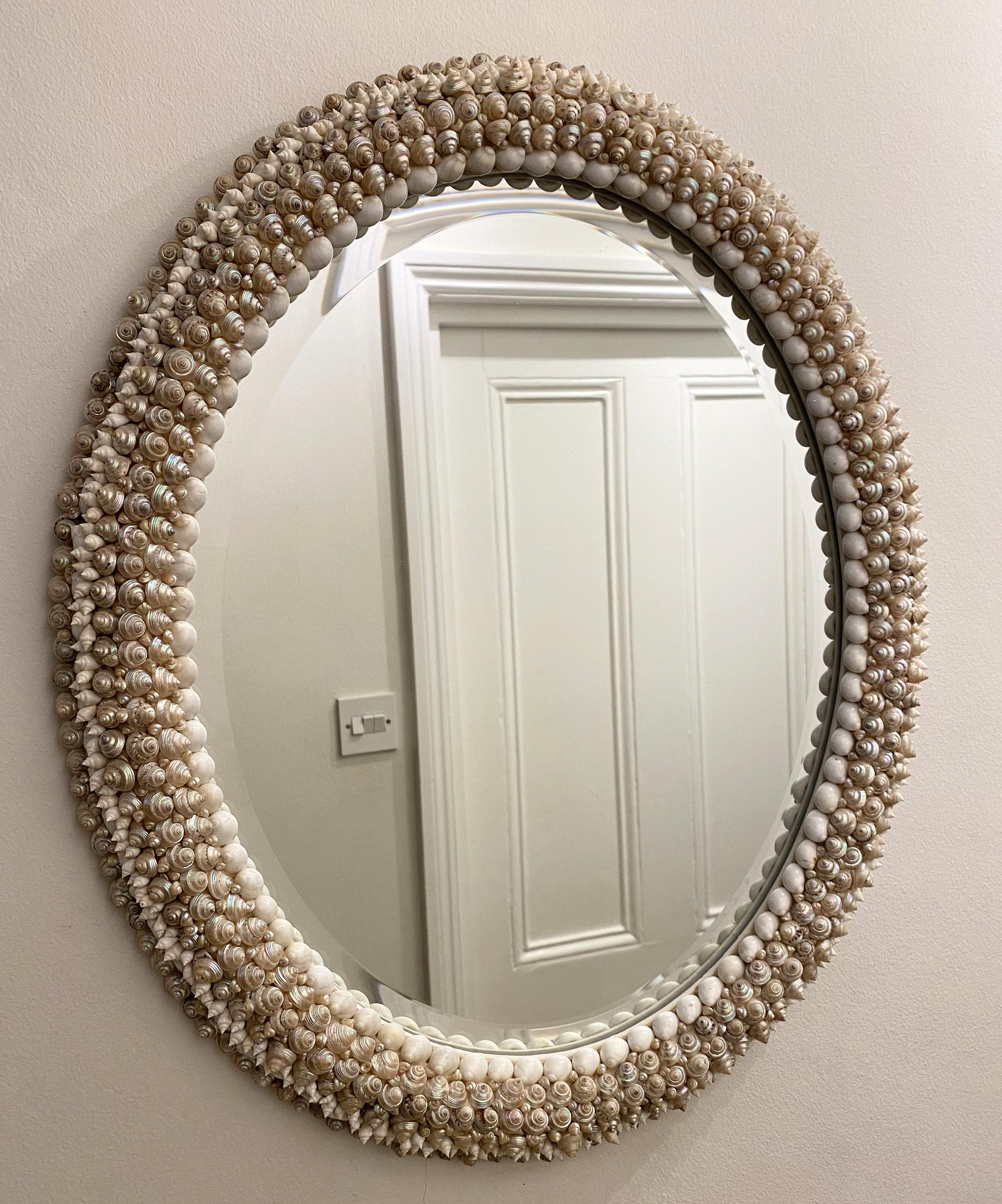 This beautiful and elegantly styled oval shell wall mirror was designed to simulate a multiple strand pearl necklace around glass with iridescent coiled shells surrounding the entire frame. The piece measures: 24 in, 61 cm high, 20 in, 50.8 cm wide