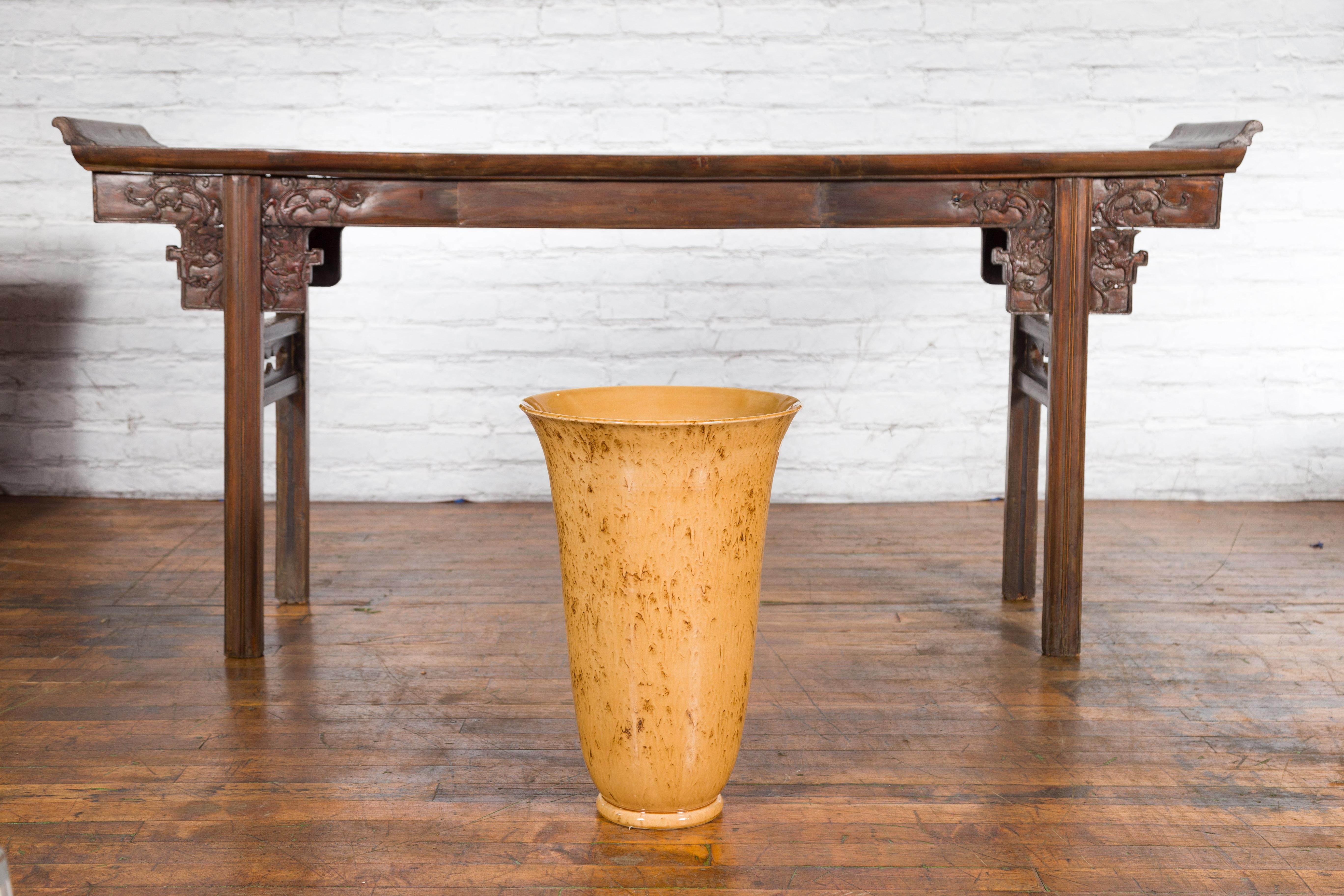 Eine große, moderne, flötenförmige Keramikvase aus der Prem-Kollektion mit gesprenkeltem Dekor und spitz zulaufender Silhouette. Diese Vase bezaubert mit ihren klaren Linien und den Gelb- und Brauntönen. Sie hat eine ausladende Öffnung mit einem