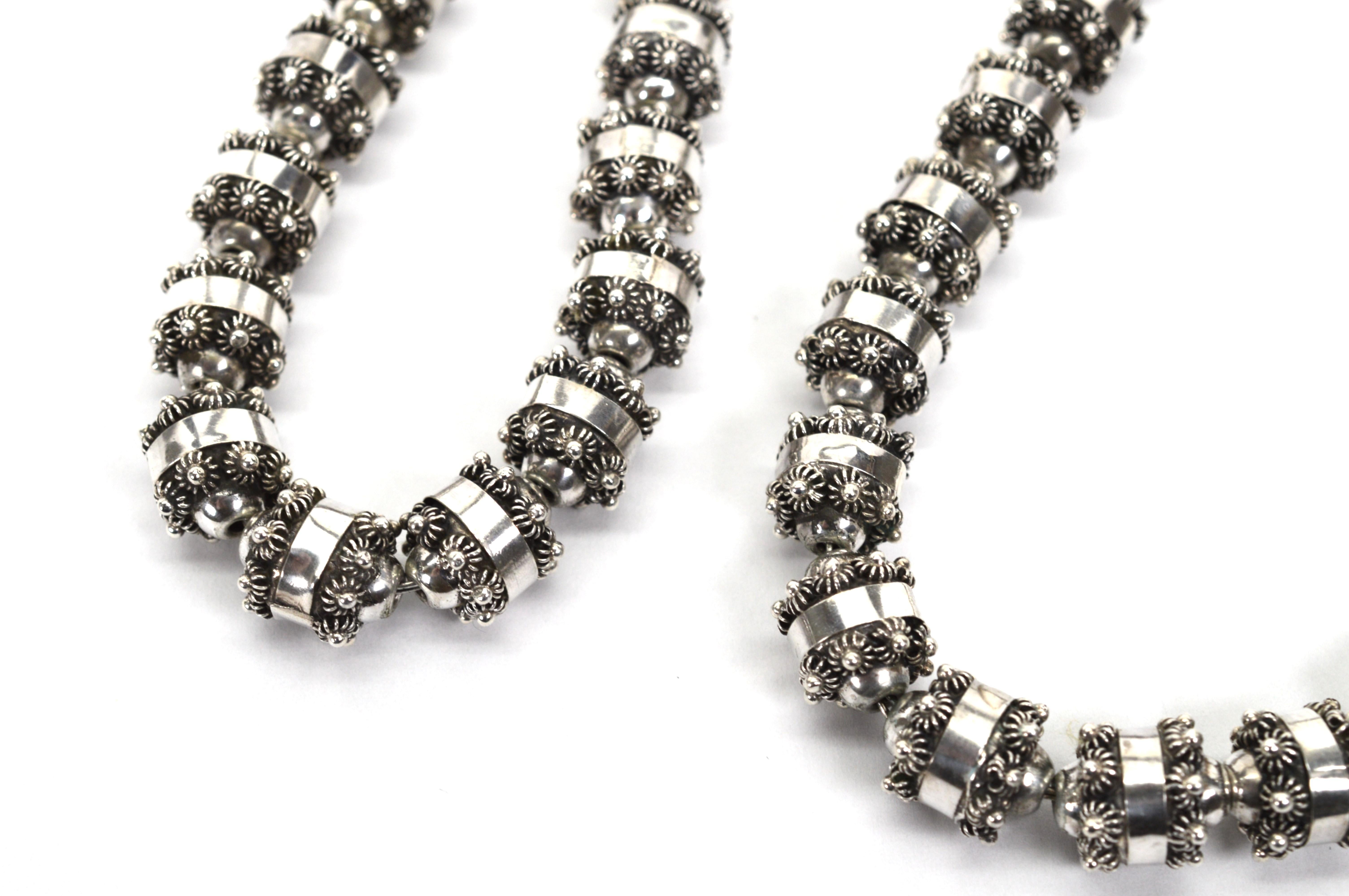 Forty eight floral-inspired uniquely shaped sterling silver beads are hand strung on durable silver chain to create a 24 inch statement necklace. Intricate artisan created tubular 10.8mm silver beads have floral blooms trimming each individual bead