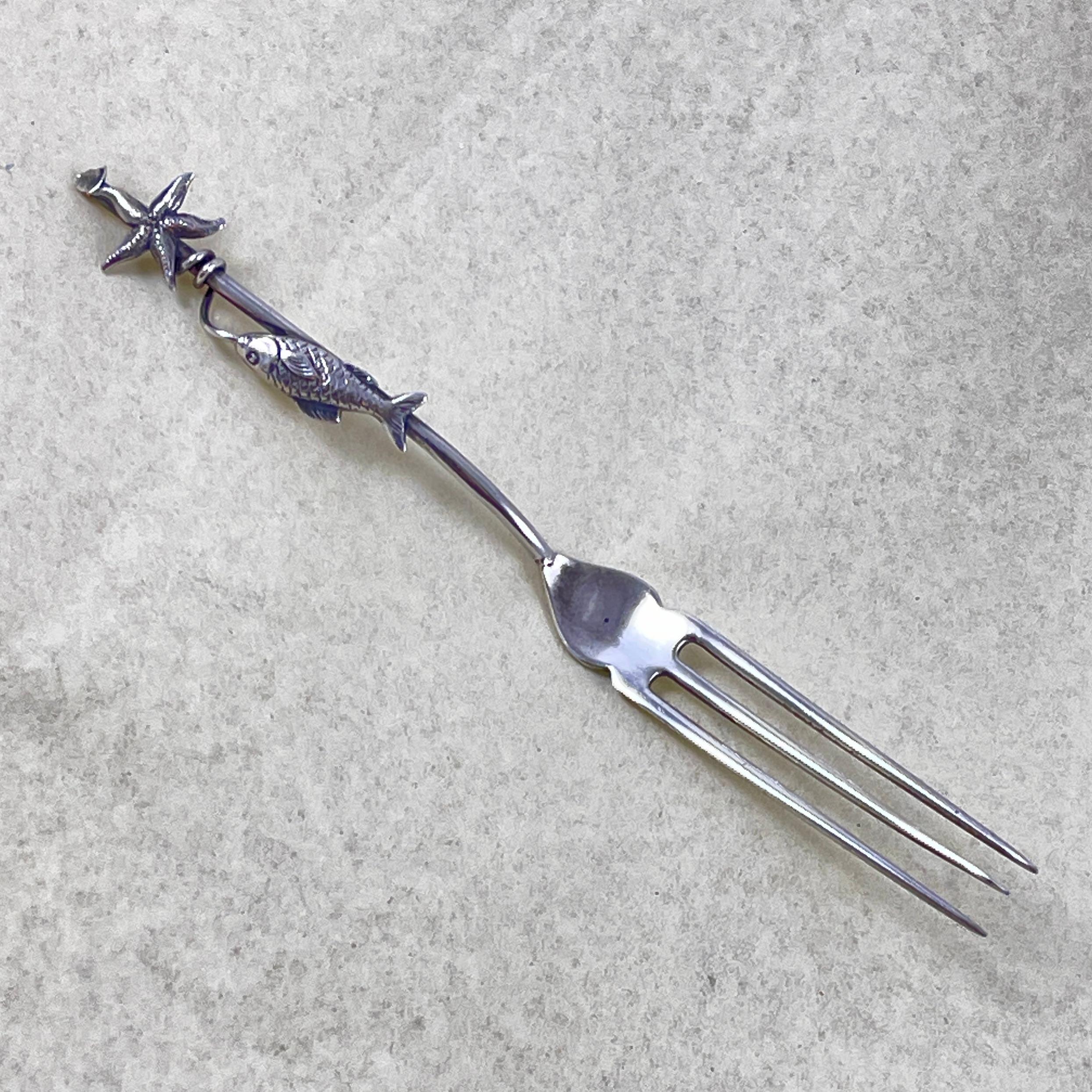 A charming one of a kind, Artisan made Sterling Silver Lemon fork with a Maritime seafood theme, circa early- mid 20th Century.

The three-tined fork features a handle modeled as a fishing pole, terminating with an applied Starfish. A fishing line