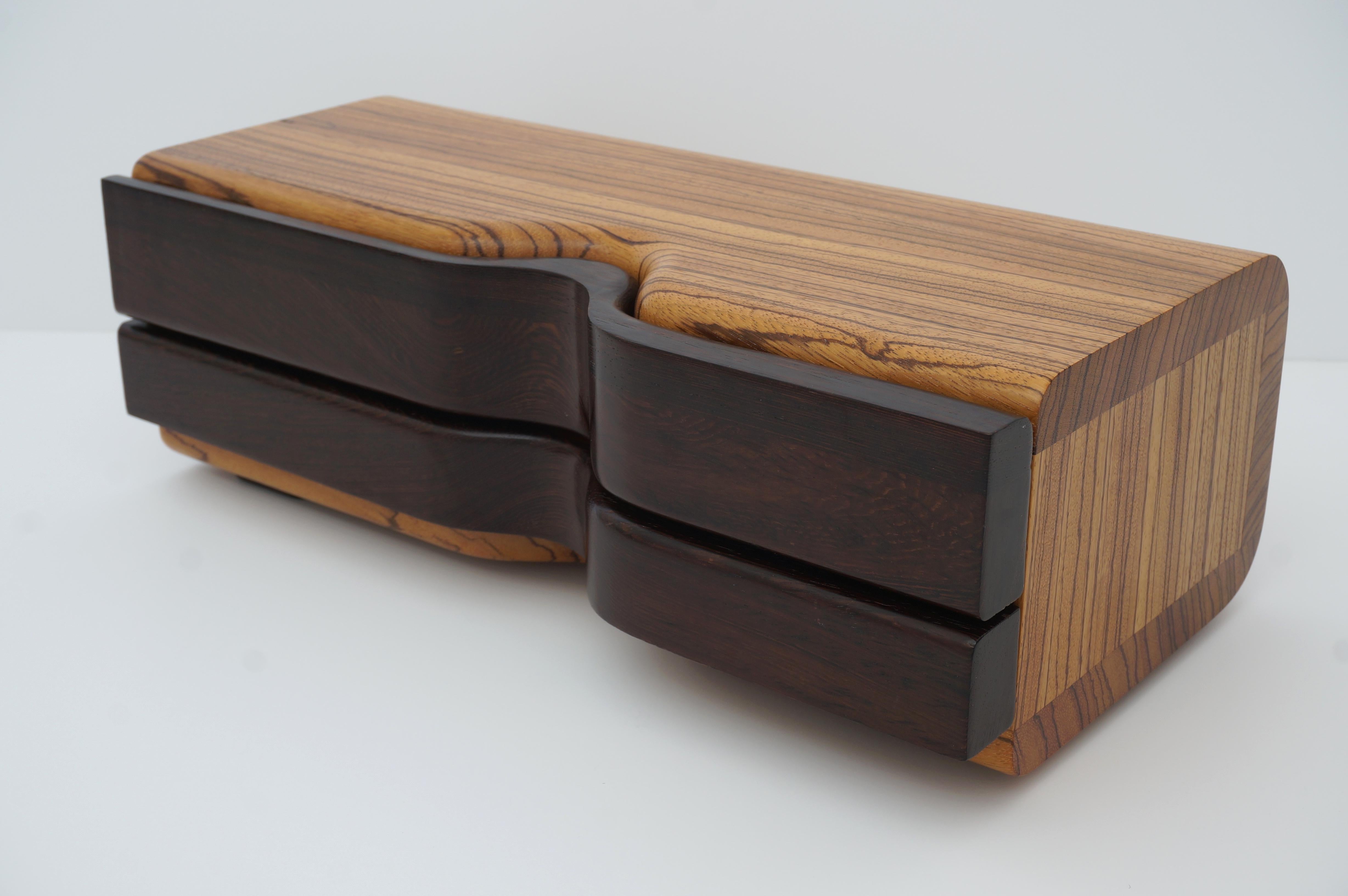 This stylish and chic artisan jewelry box will make a beautiful addition to your dressing table. The piece is created using an exotic mix of solid woods to create a visually intoxicating form and finish.