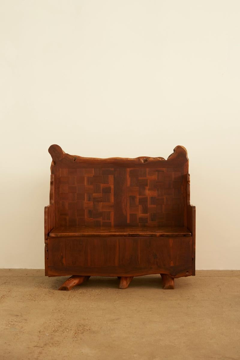 Un banc très unique en bois d'olivier à l'esthétique artisanale, avec un dossier en bois tressé, des bords sculptés et des détails en grain de bois naturel. La conception robuste comprend un compartiment de rangement sous le siège, ce qui le rend à