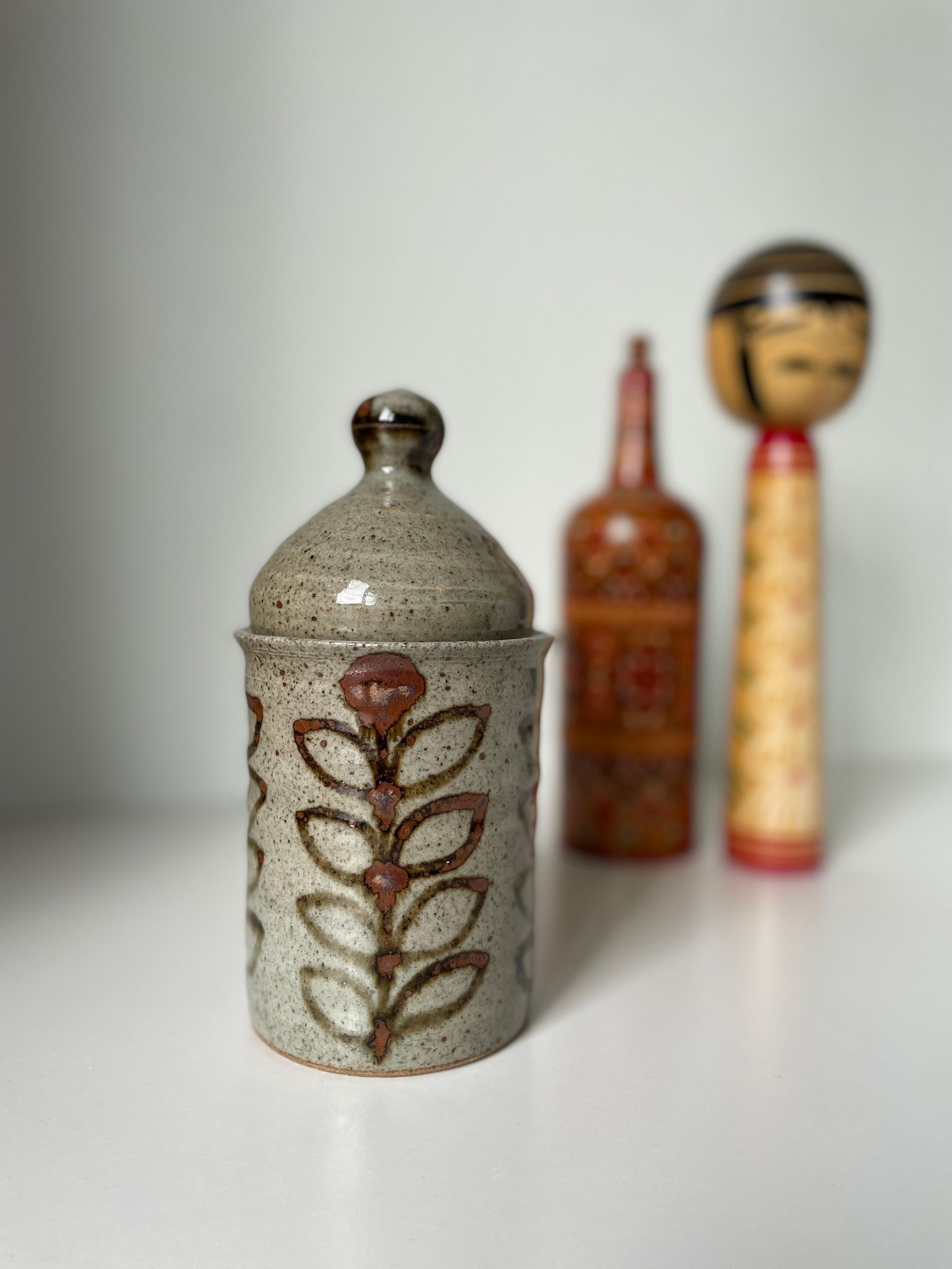 Französischer handwerklicher Vintage-Keramikzylinder mit weich geformtem Deckel. Handgemalte stilisierte Blumendekorationen in rostbraunen Farben auf der sandgrauen, glänzenden Glasur. Unter dem Sockel gestempelt und signiert. Schöner