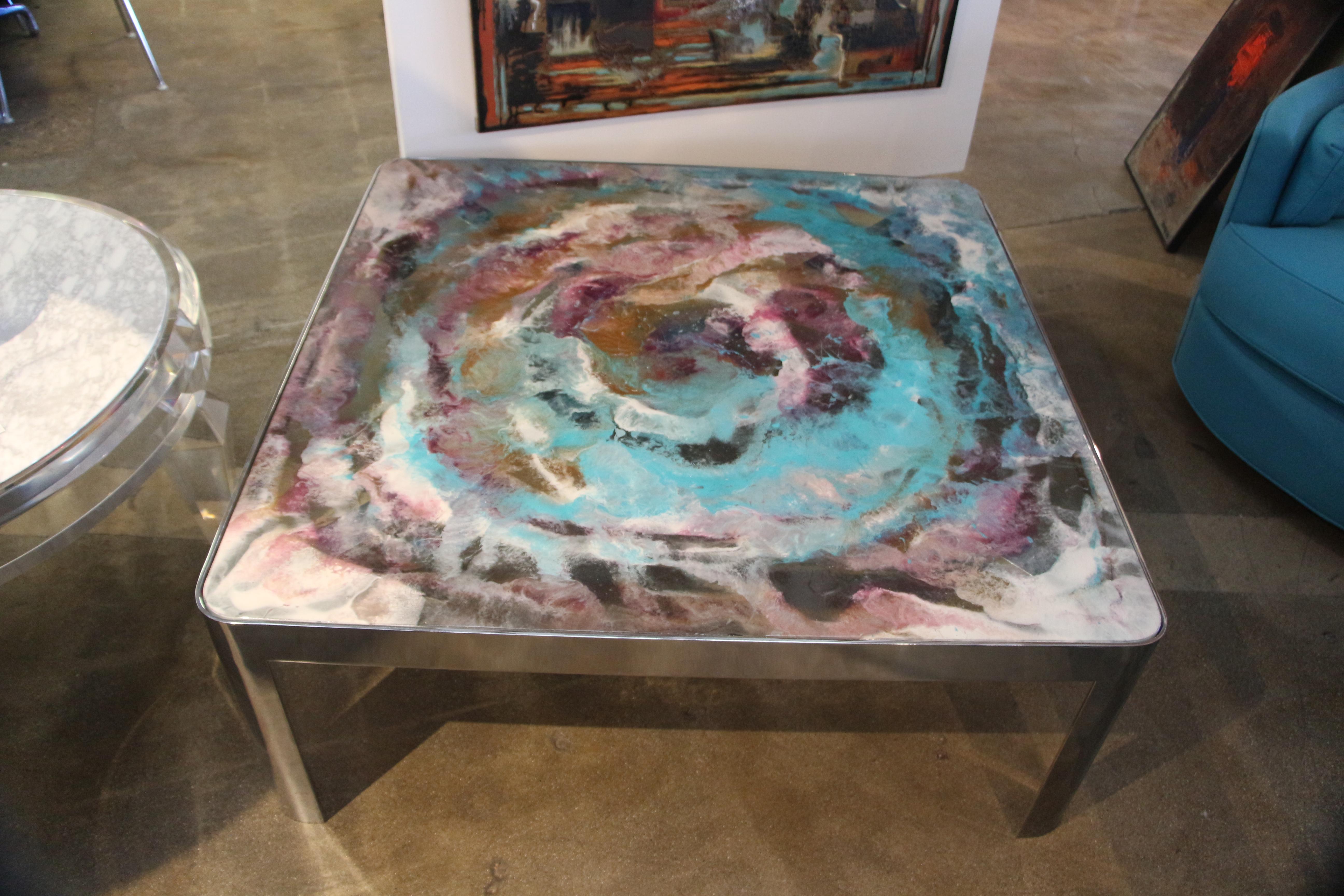 Artist, Marco Antonio, used the glass top of this table to paint a beautiful abstract. it is Epoxy paint decorated glass top on a Vintage 1980s chromed steel base. The abstract art top is colorful and vibrant.
There are some minor marks on the base