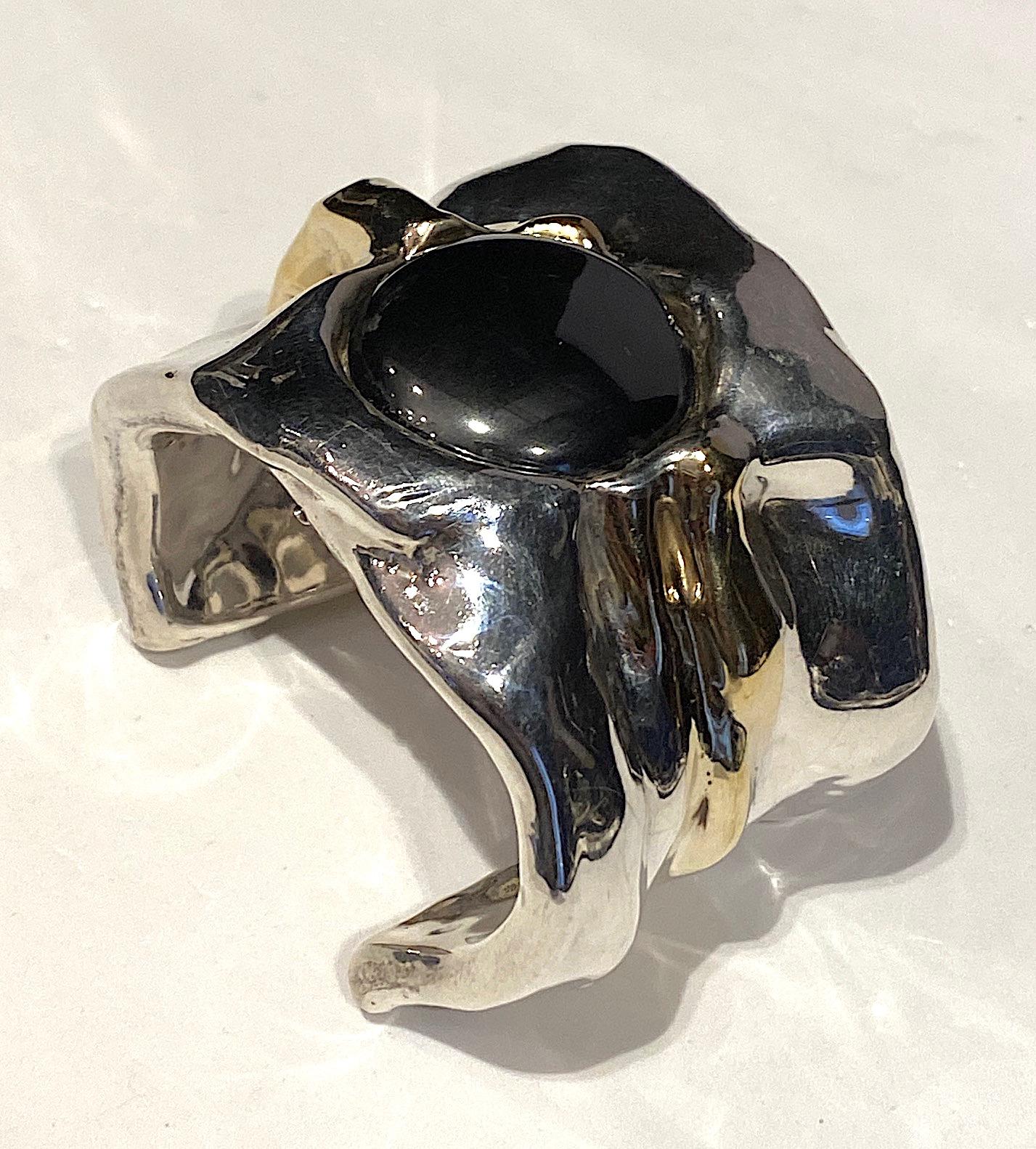 A 1980s artist made and signer wide cuff set with a 1.25 inch diameter hematite cabochon. The cuff is 2.25 inches wide, up to a half in thick in areas and 6.5 inches long with a 1.5 inch opening. It is stamped on the back 925 for sterling silver and