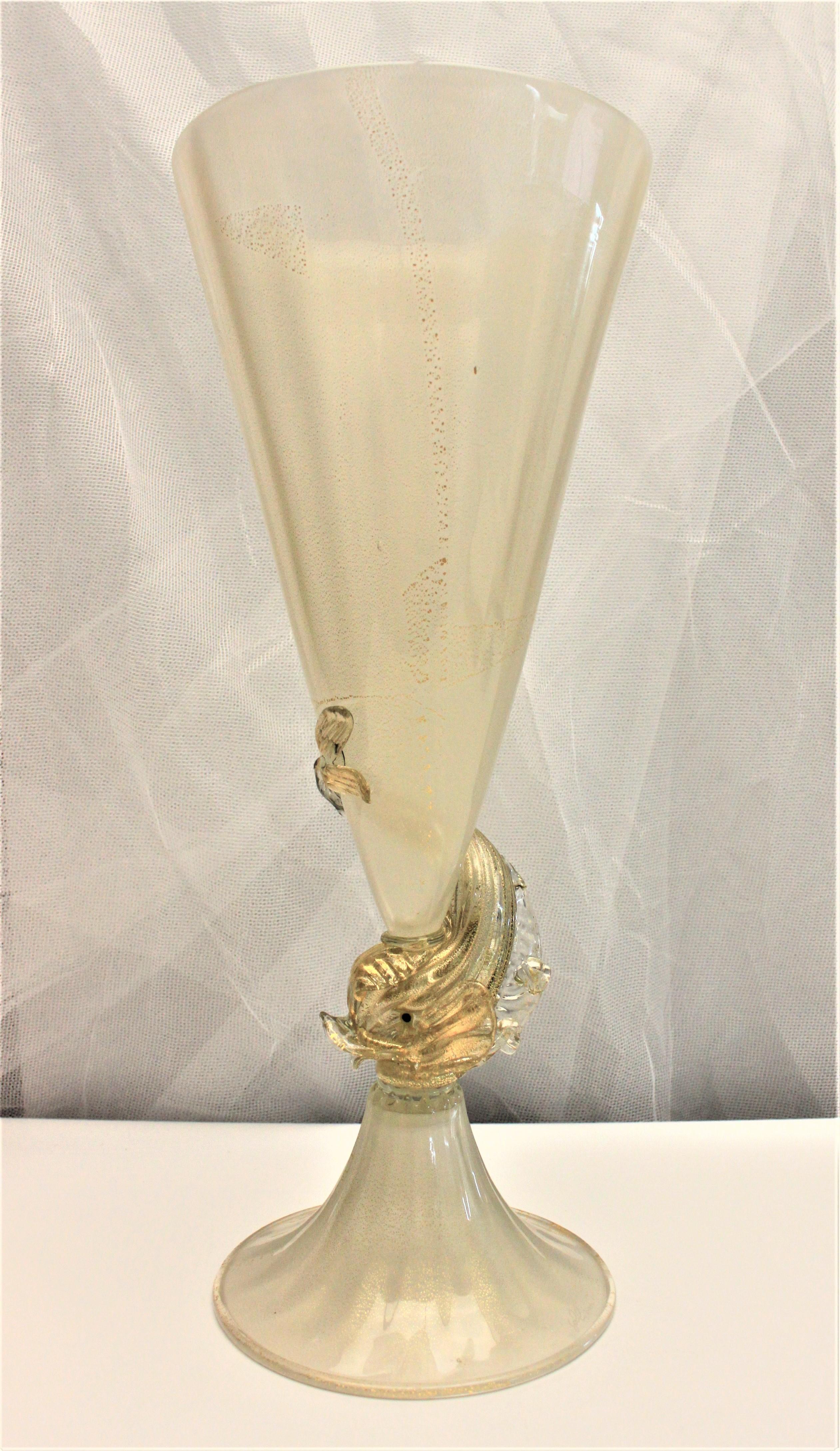 This Mid-Century Modern art glass Murano vase is Artist-signed at the base, but the signature is illegible, so the exact artist cannot be determined. The trumpet style vase is done in a somewhat opaque base glass with heavy flecks of gold, or