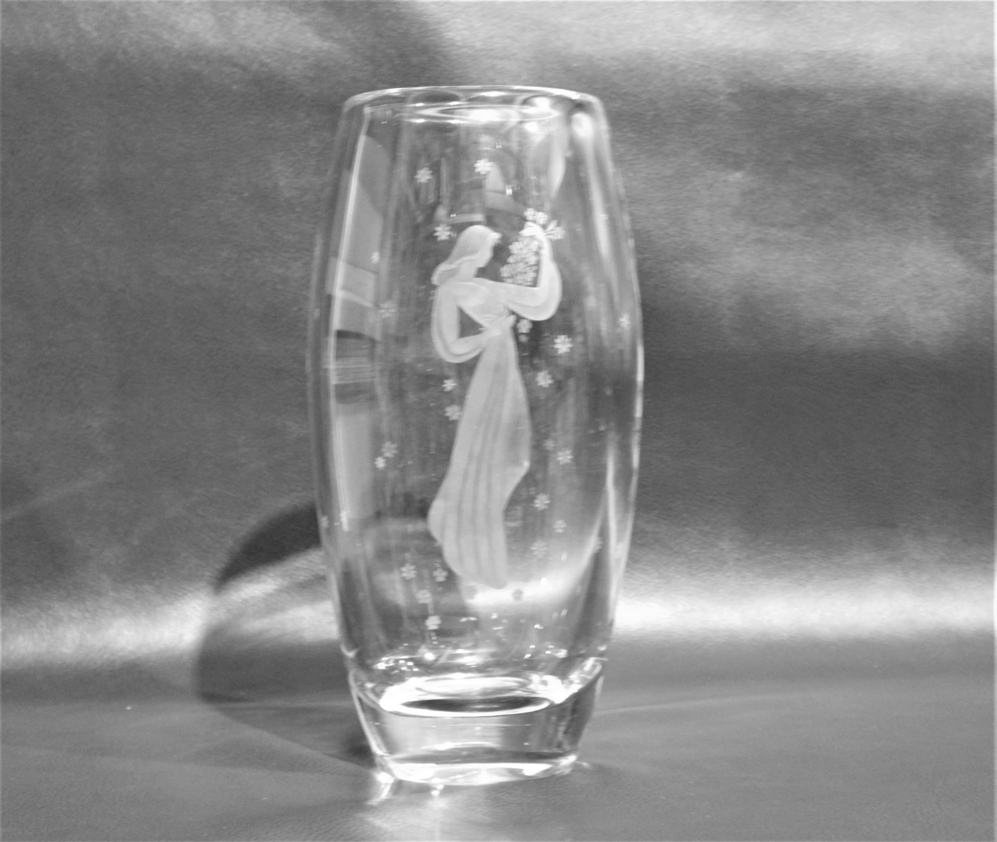 This large signed Orrefors crystal vase was made in Sweden during the 1970s in a Mid-Century Modern style and stands almost a foot tall. The vase depicts a stylized maiden holding a bouquet of flowers with a series of stylized flowers that