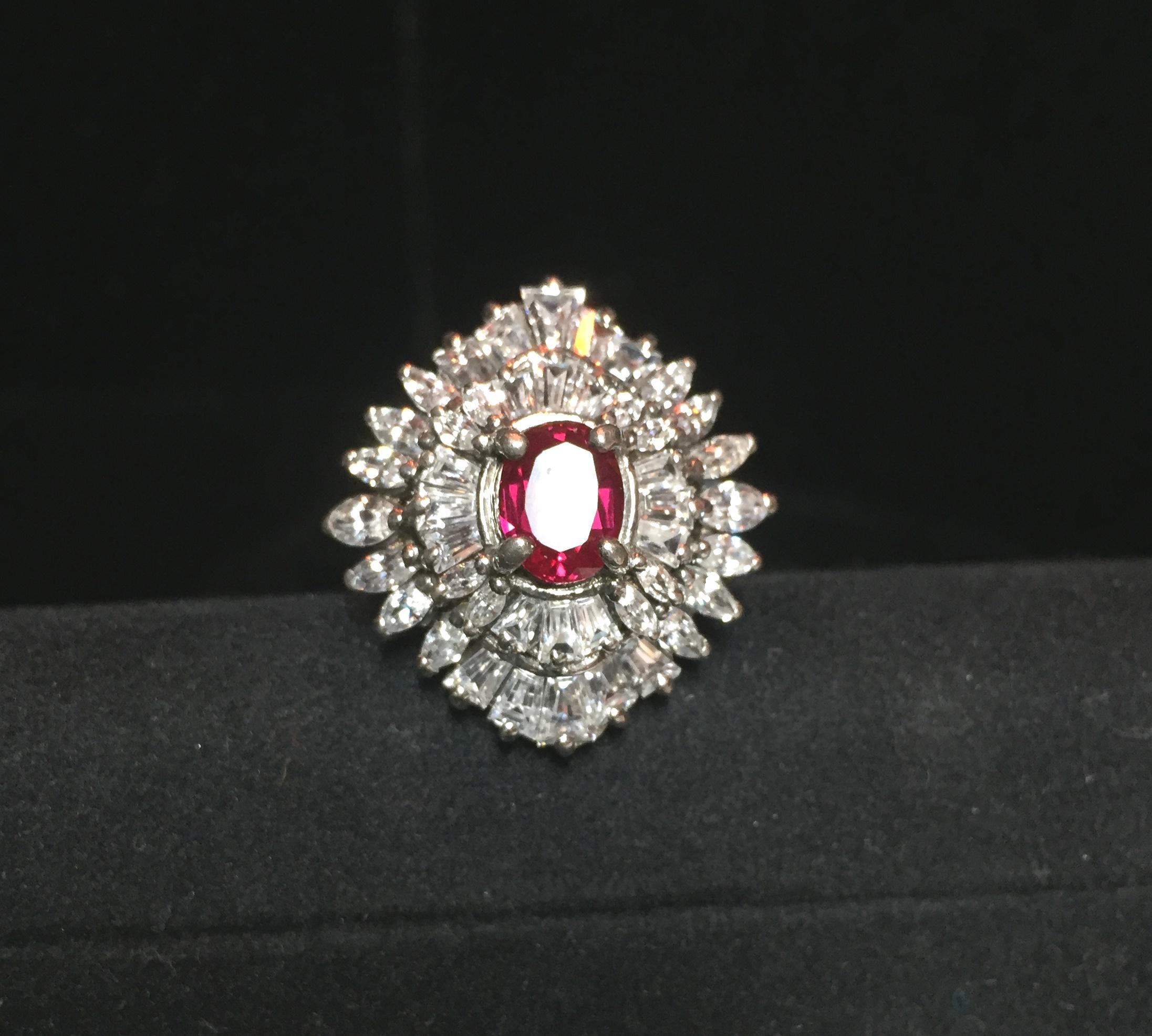 Offered here is an artist-signed sterling silver, cubic zirconia, & synthetic ruby cocktail ring from the 1970s. The traditional stepped design presents two tiers of ice-clear cubic zirconia in marquise and tapered baguette cuts, leading up to a