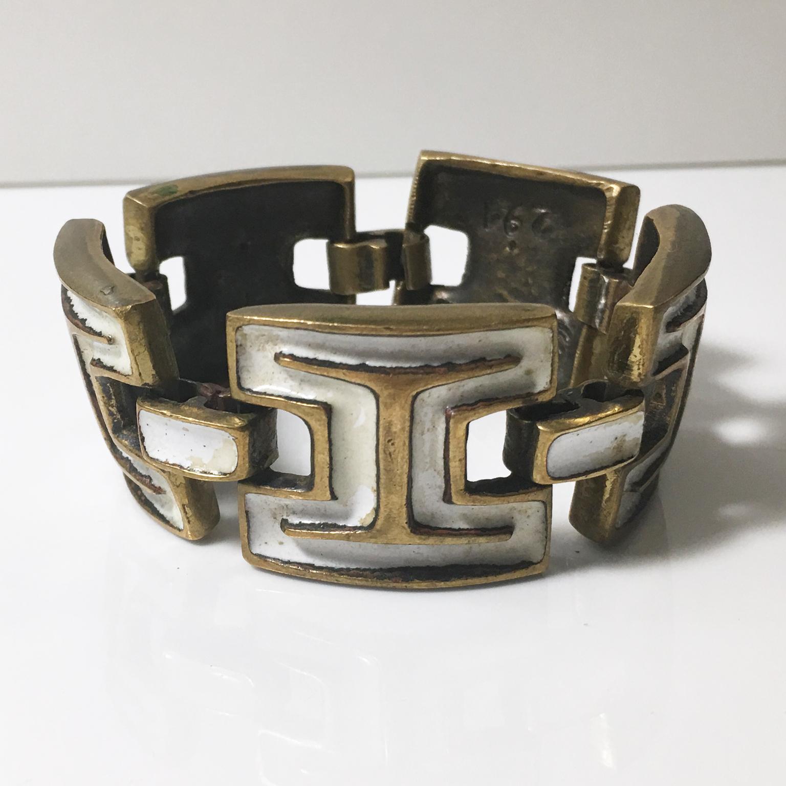 This is a stunning Mid-Century modernist bronze and enamel link bracelet designed by French artist St Luc. The piece features geometric gilded bronze metal carved elements topped with white enamel. The bracelet has a hook-closing clasp. The