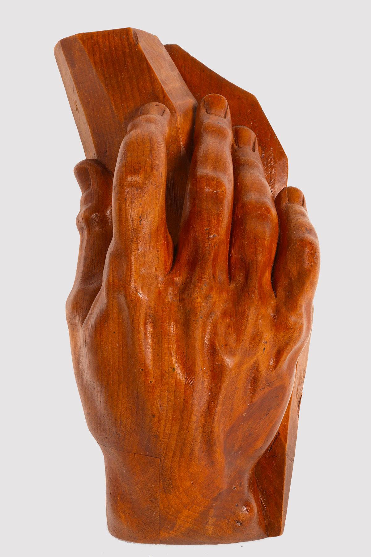 Scultura artistica dell'Atelier A raffigurante una mano maschile. Realizzata in legno di frutta, la scultura ha una base liscia con un bordo geometrico irregolare, su cui si trova la prova dell'artista di una lavorazione raffinata e realistica,