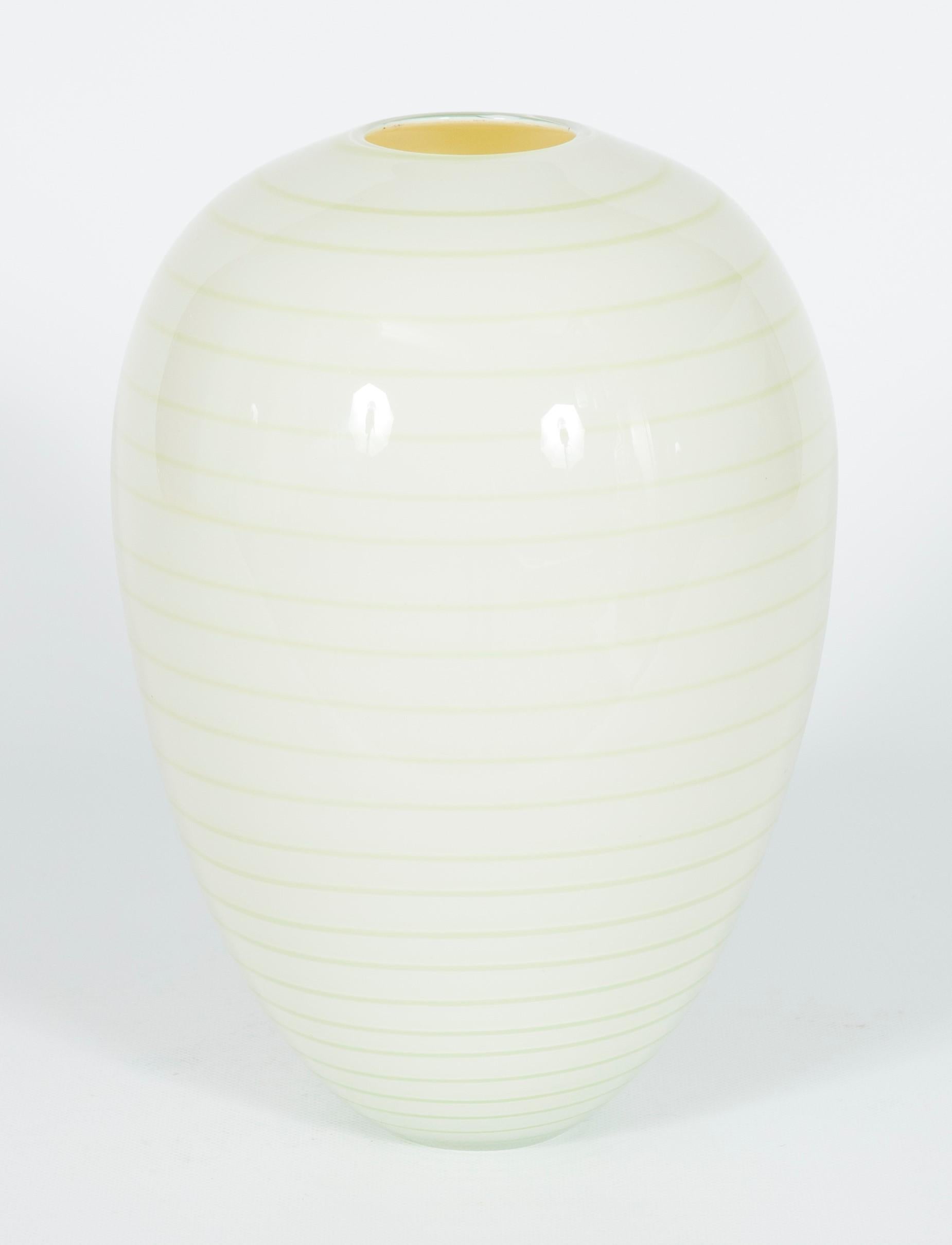 Artistic ornament vase in white Murano glass, attributed to Seguso, 1960s.
The harmoniously rounded oval shape, the delicate cream-white color, and the horizontal green strips made with sunken glass canes give a true touch of Italian creativity and