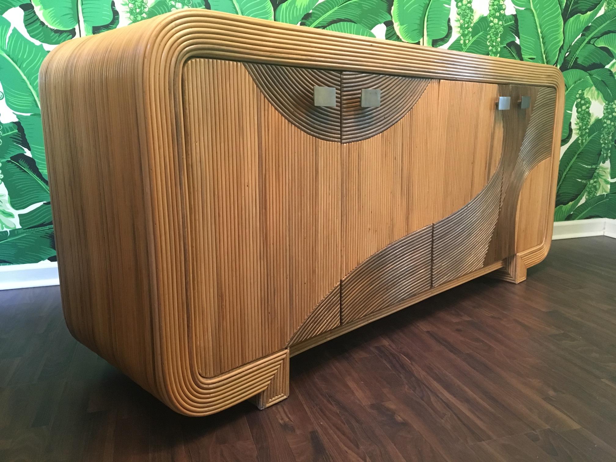 One of a kind wrapped rattan buffet features artistic split reed detailing formed into an asymmetrical wave pattern. Detailed pattern even continues inside doors. Bronze hardware and removable shelving. Used as a credenza or server, a definite